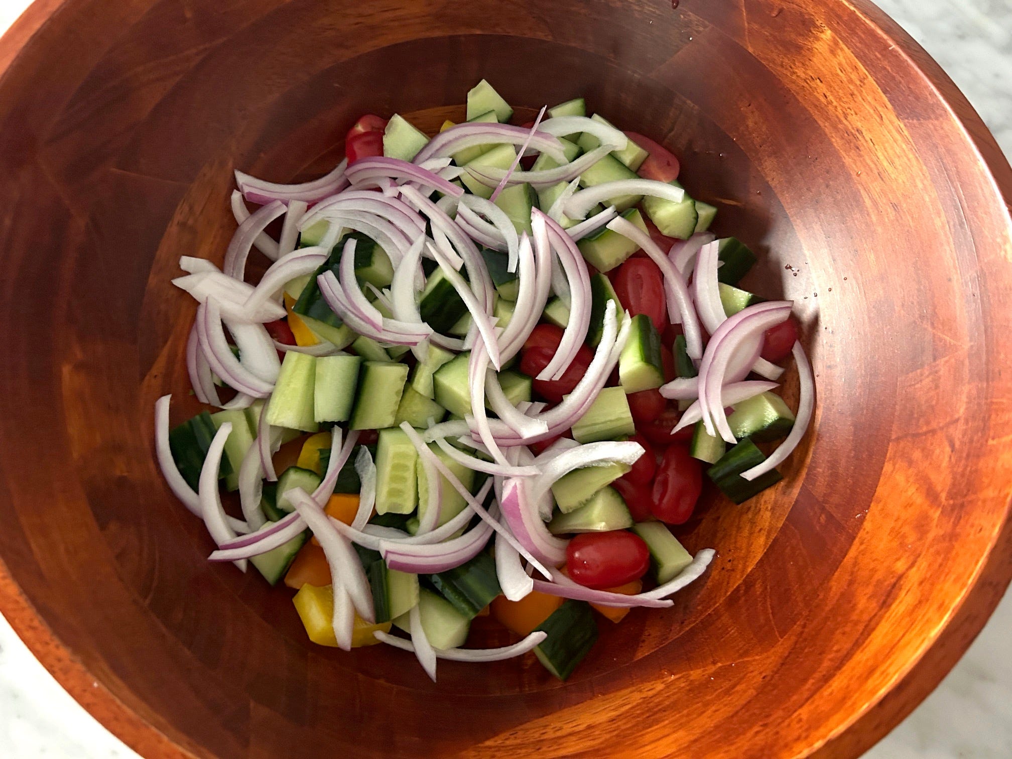 Adding chopped veggies to a bowl for Ina Garten's Greek panzanella salad