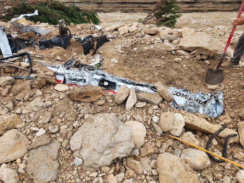 Wreckage of a vehicle in a rocky area near a river.