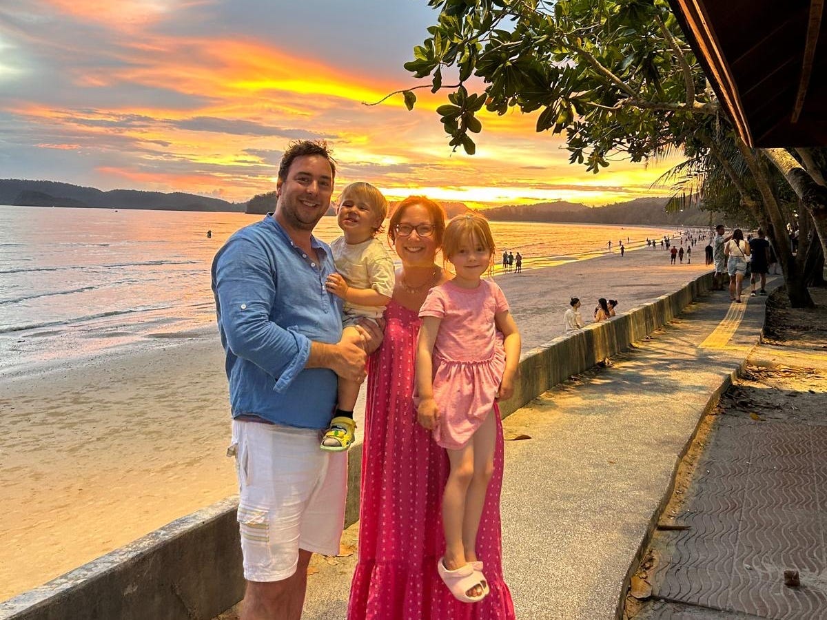 A family of four poses near the water during sunset.