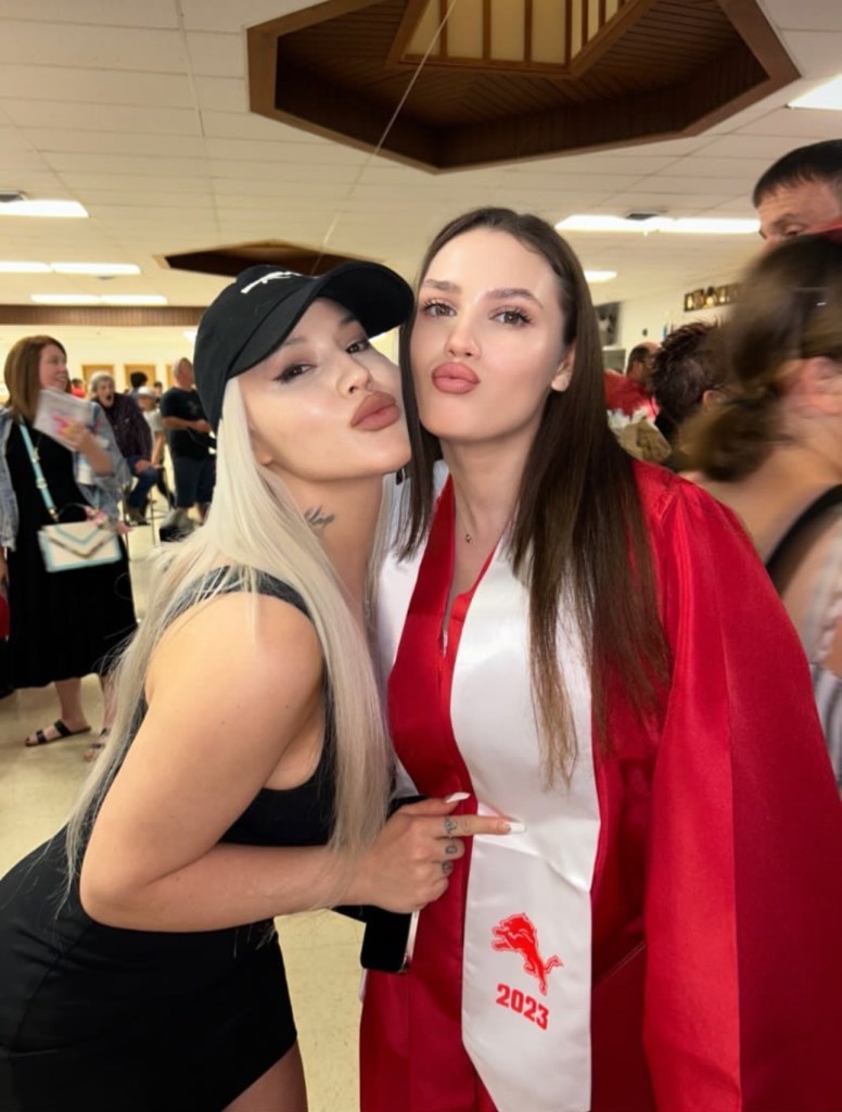 Two women posing for a photo; one is wearing a black dress and the other is wearing a red graduation gown.