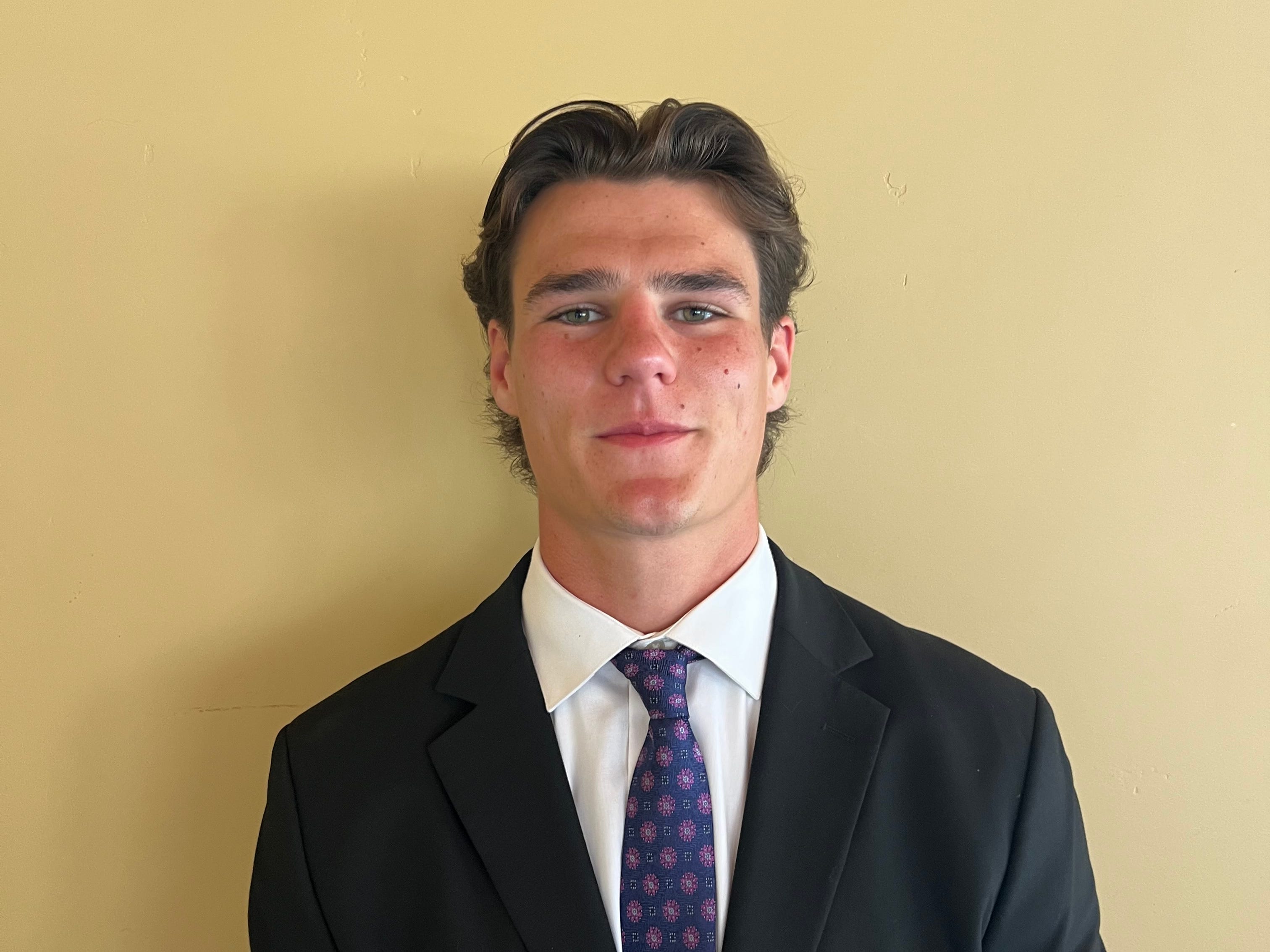 Headshot of intern in a suit standing in front of yellow background