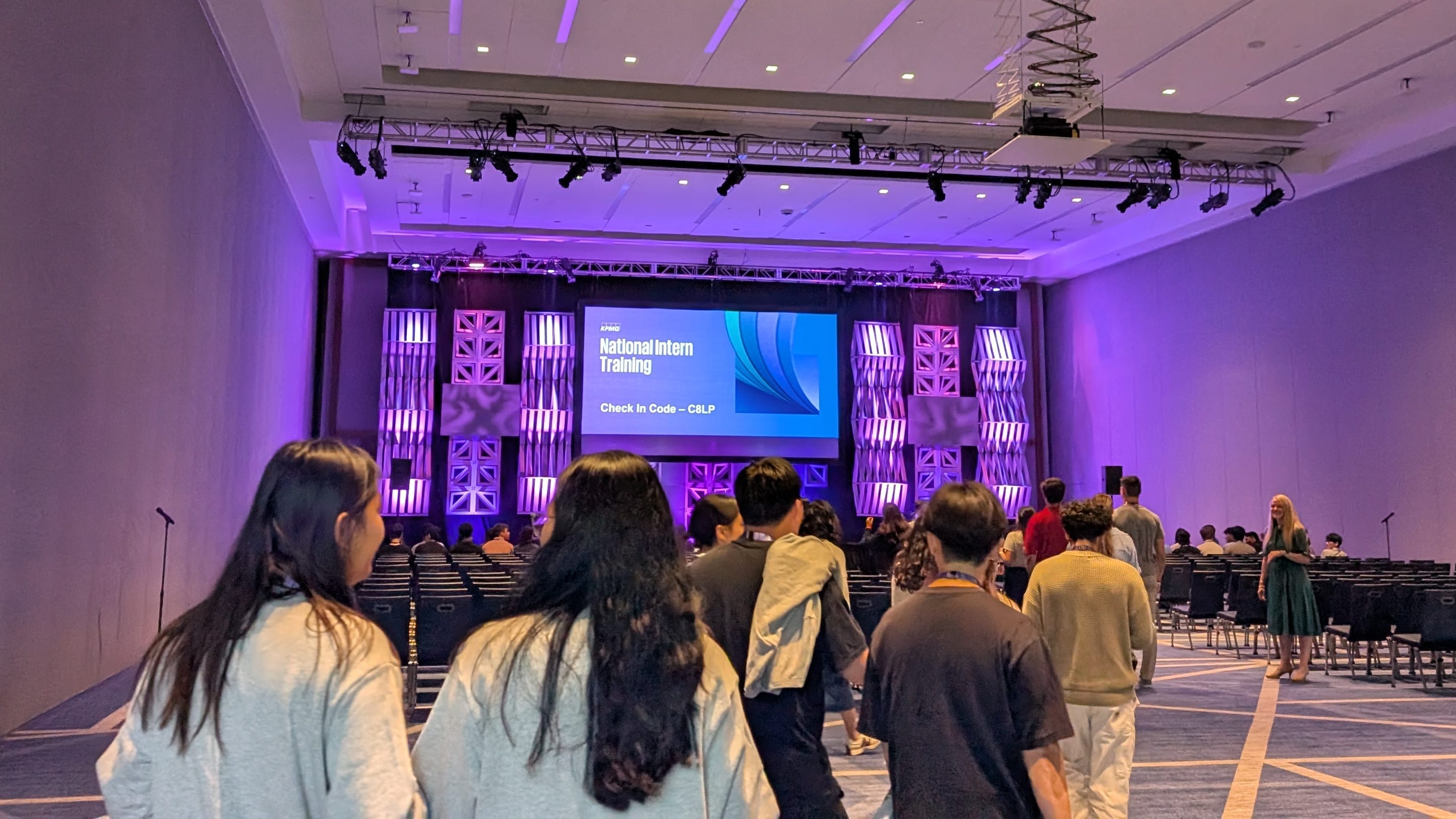 KPMG interns arrive at a welcome event in a hall with a purple screen.