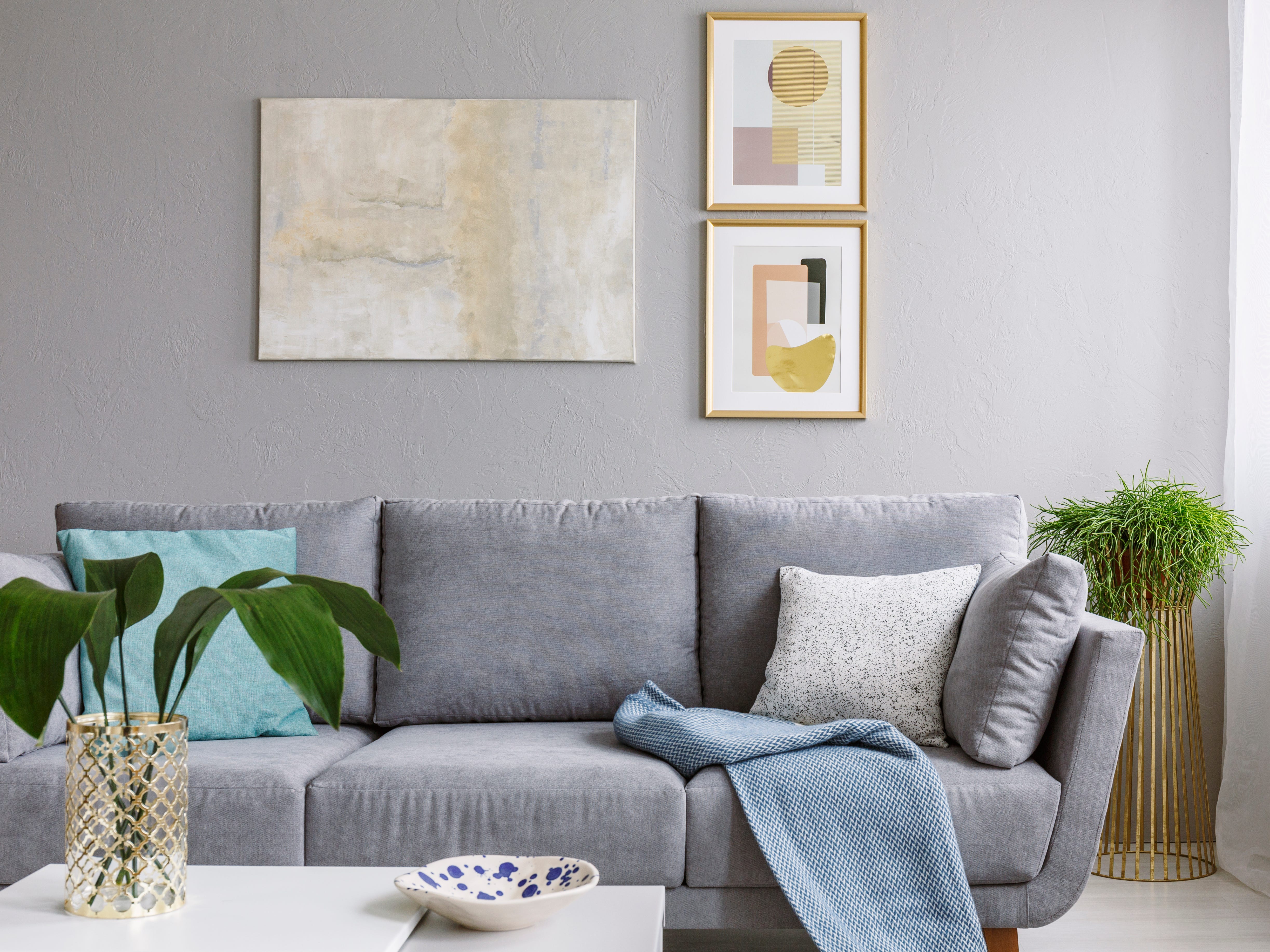 Three paintings on a gray wall in a living room with a gray couch.
