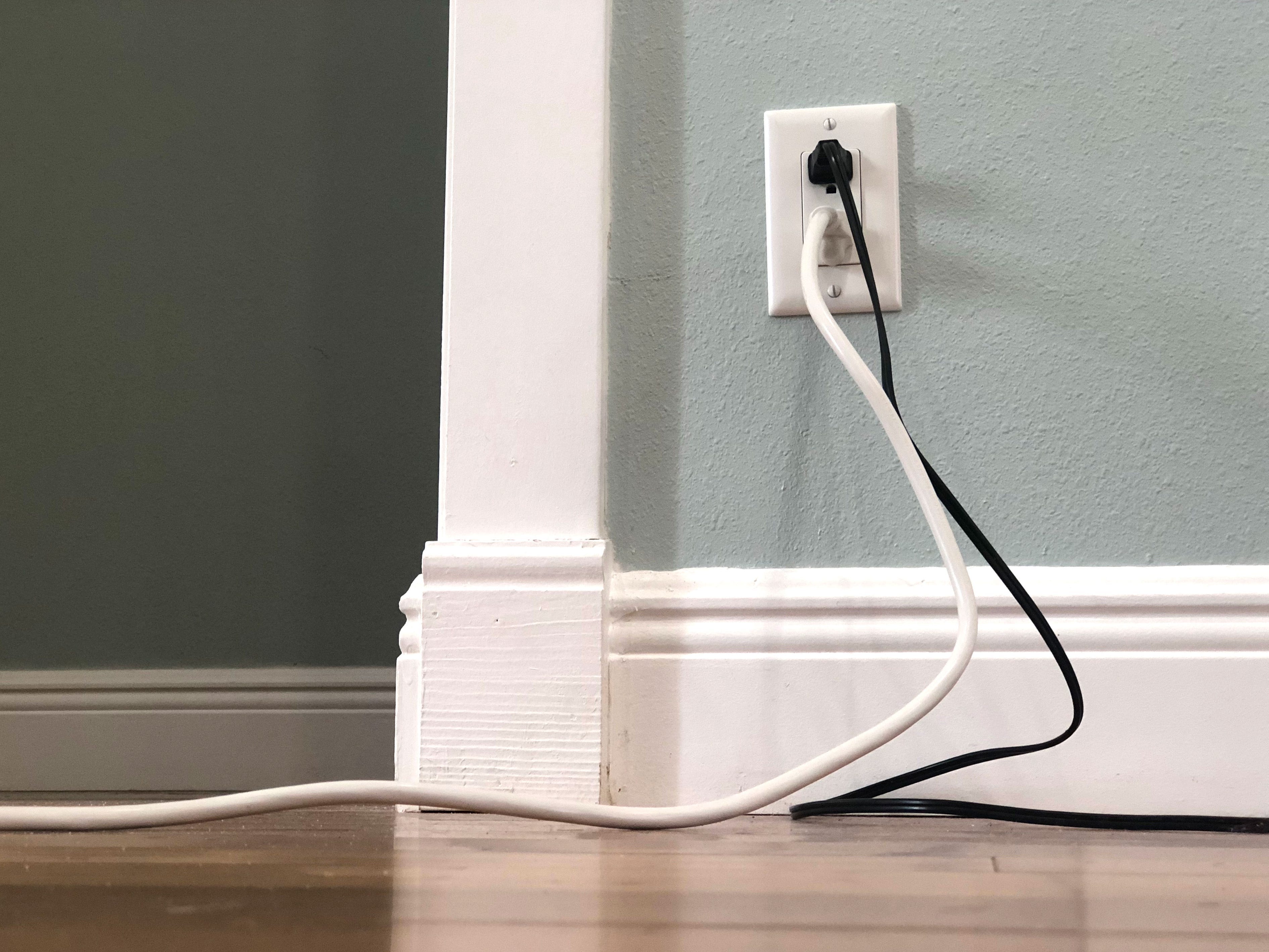 Two chunky cords plugged into an outlet on a green wall.