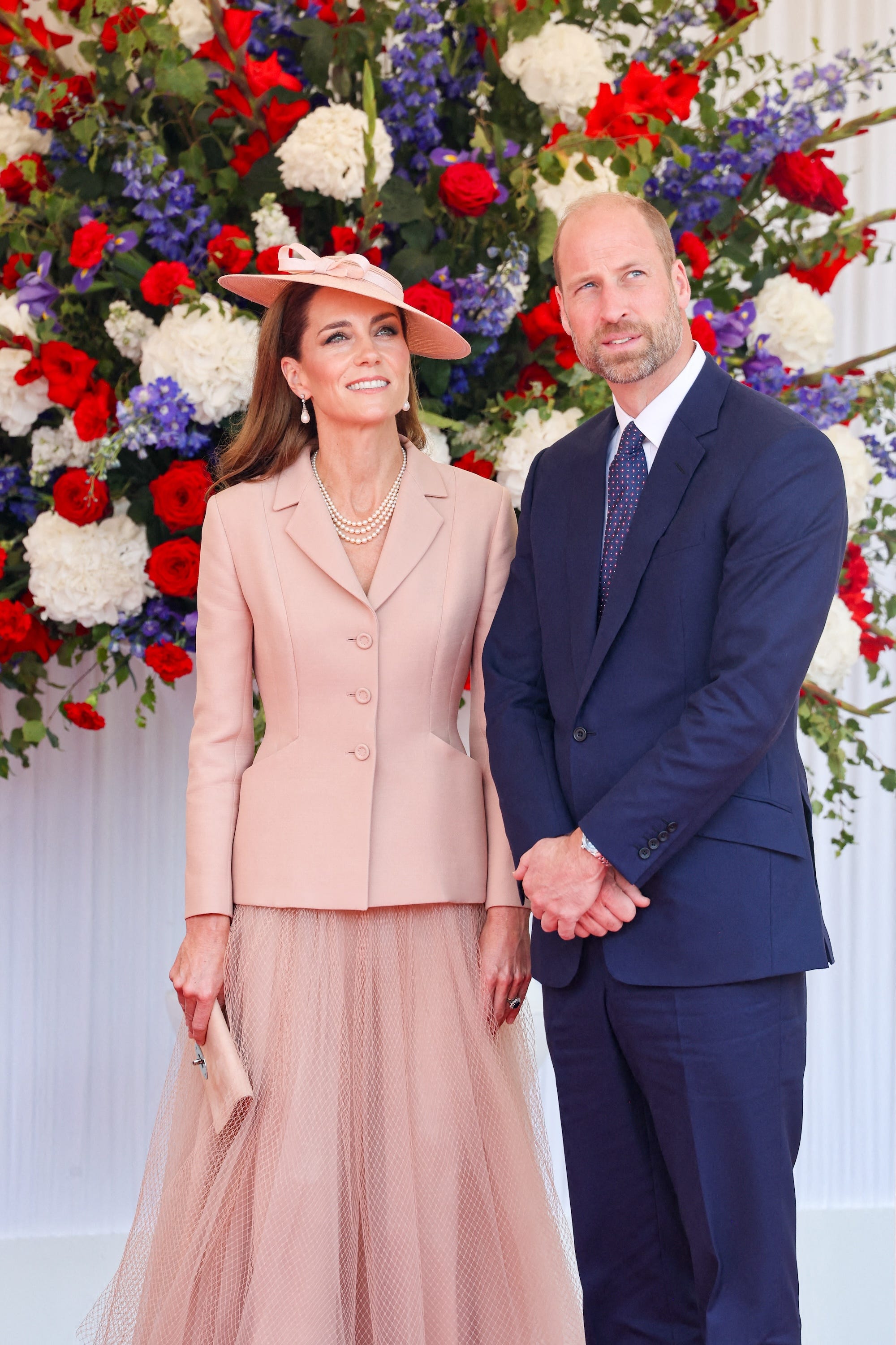 Kate Middleton and Prince William stand in front of a colorful floral display.