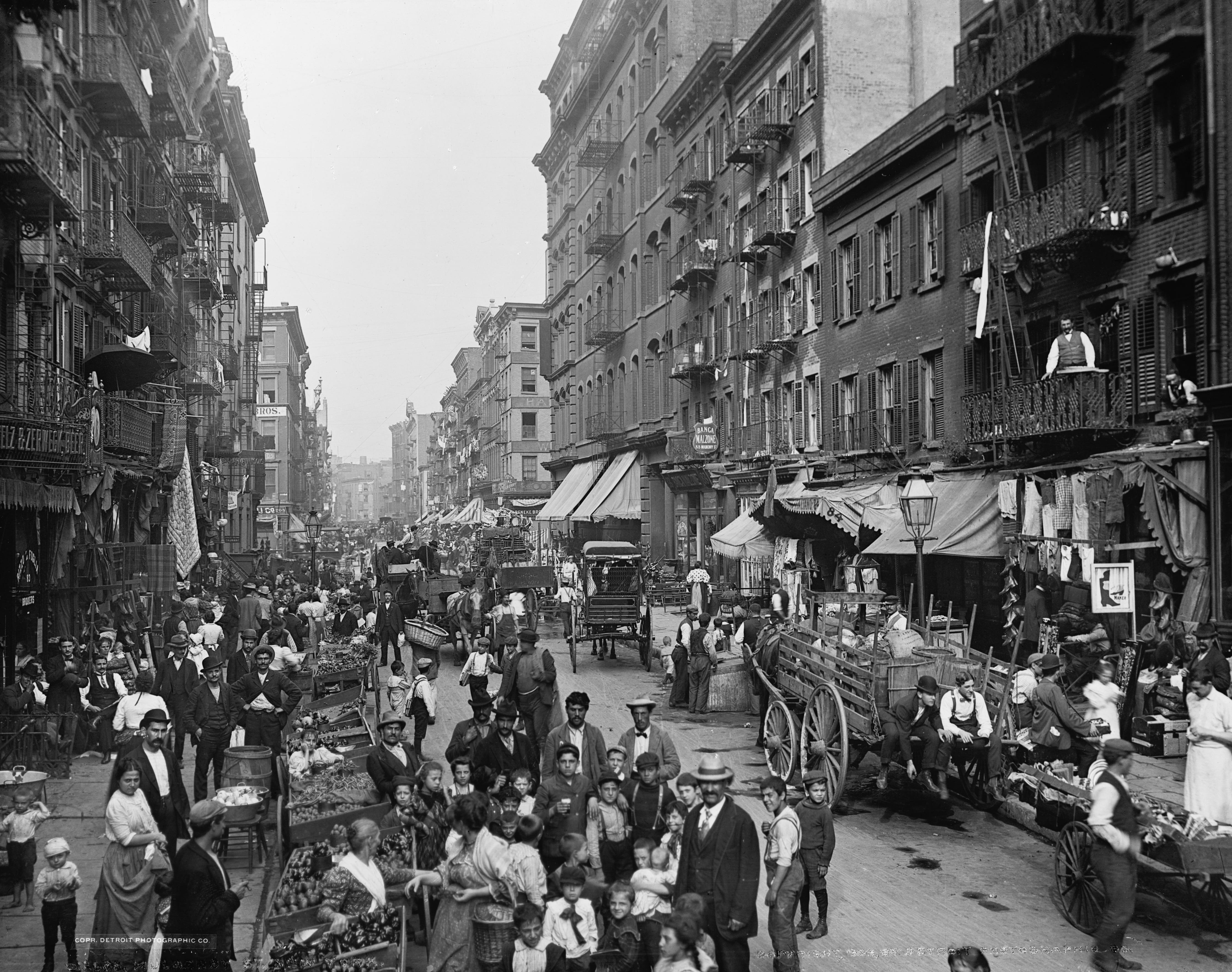 Street scene showing pedestrians, shoppers, and merchants with their vendor carts and stalls, on Mulberry Street, New York, circa 1900.