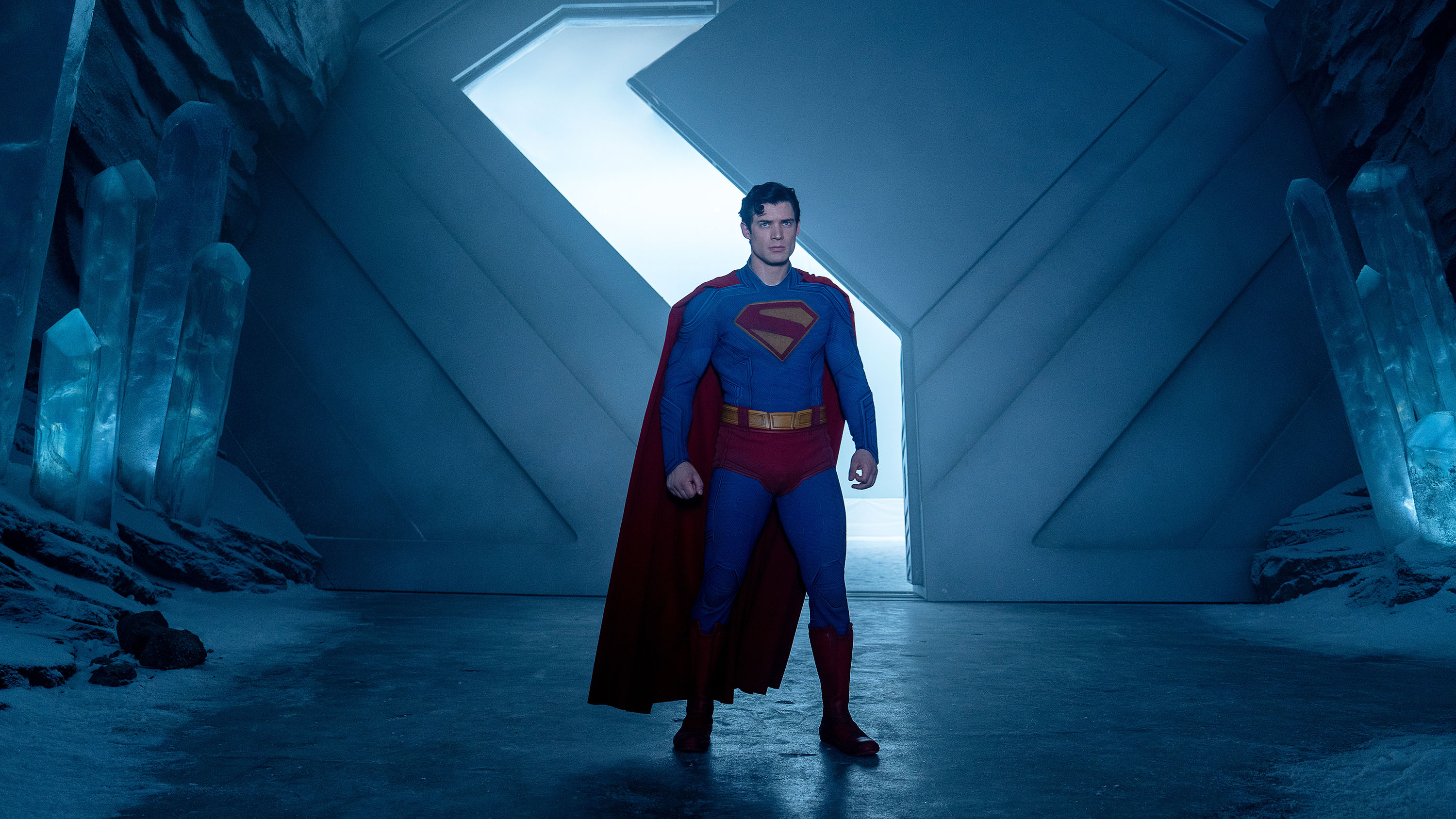 A color photograph of Superman in a cavelike room, with a zigzagged door open behind him.