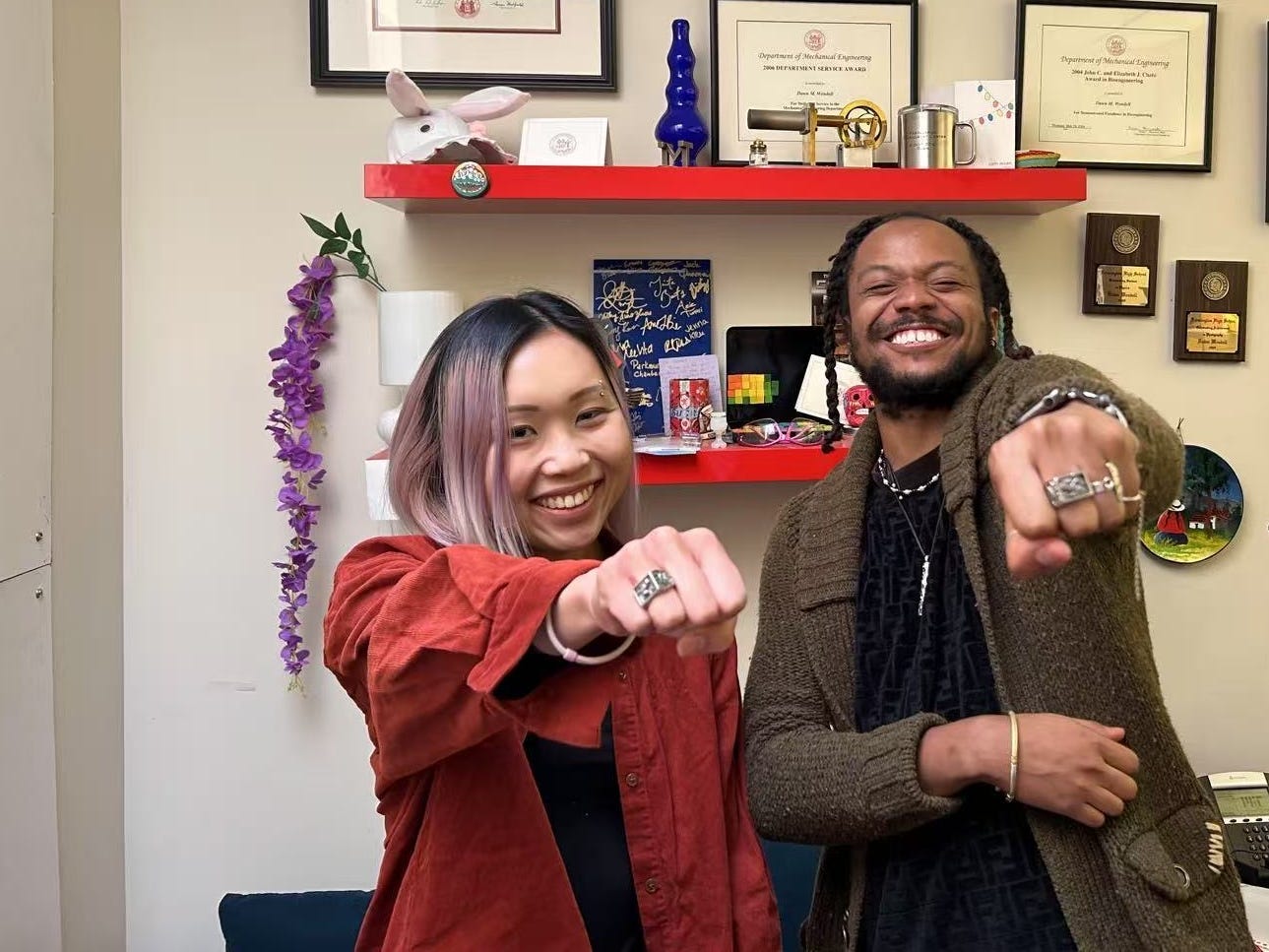 Two MIT graduates showing off their "brass rat" class rings.