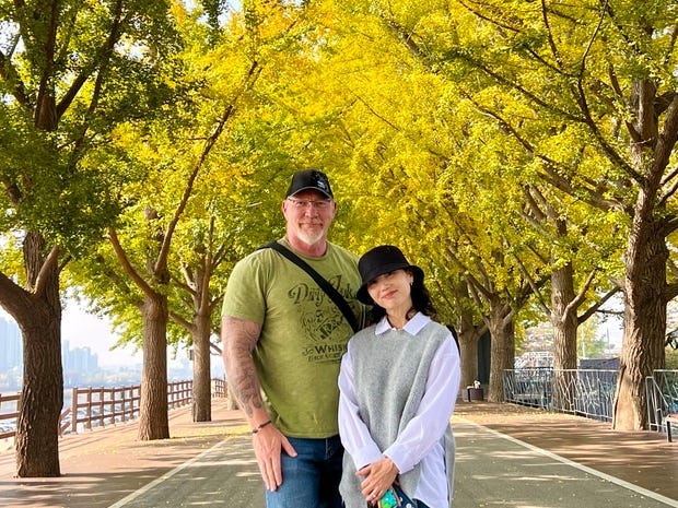 A couple posing in the middle of a street, surrounding by trees.