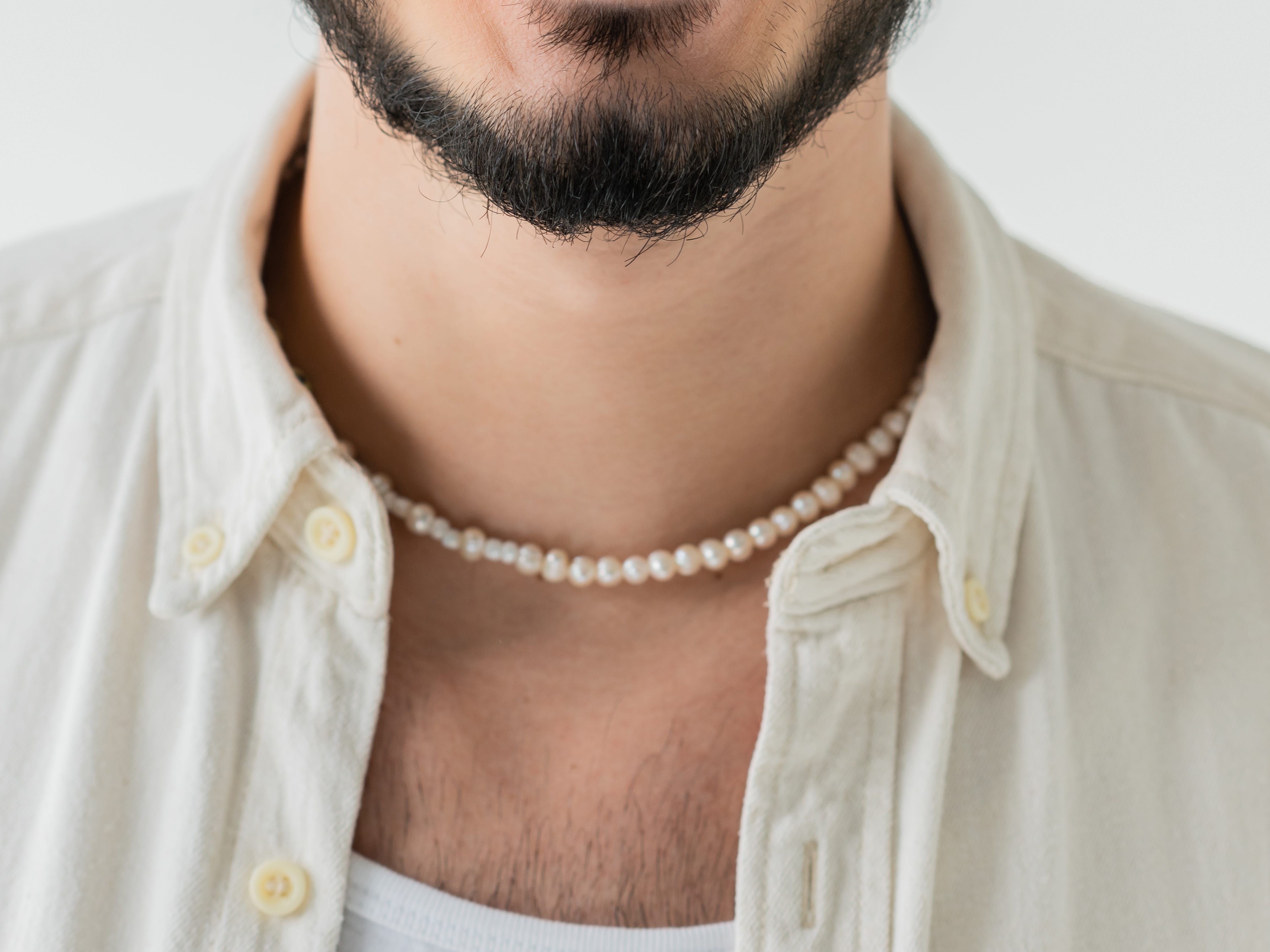 headshot of a man wearing a neutral outfit with a single strand of peal necklace