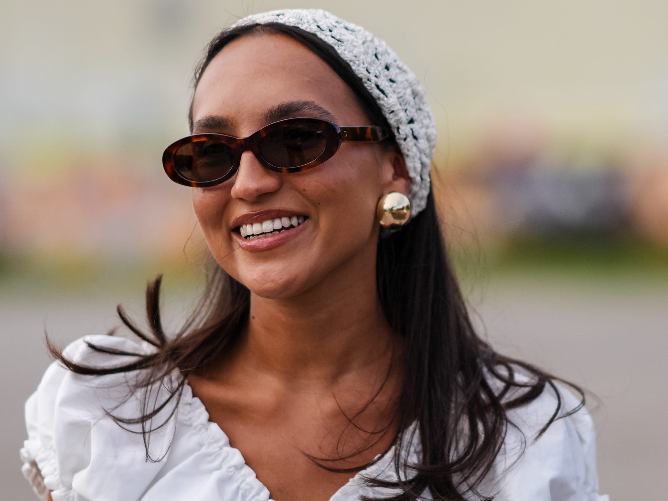 woman wearing a white outfit with a headband and big gold earrings