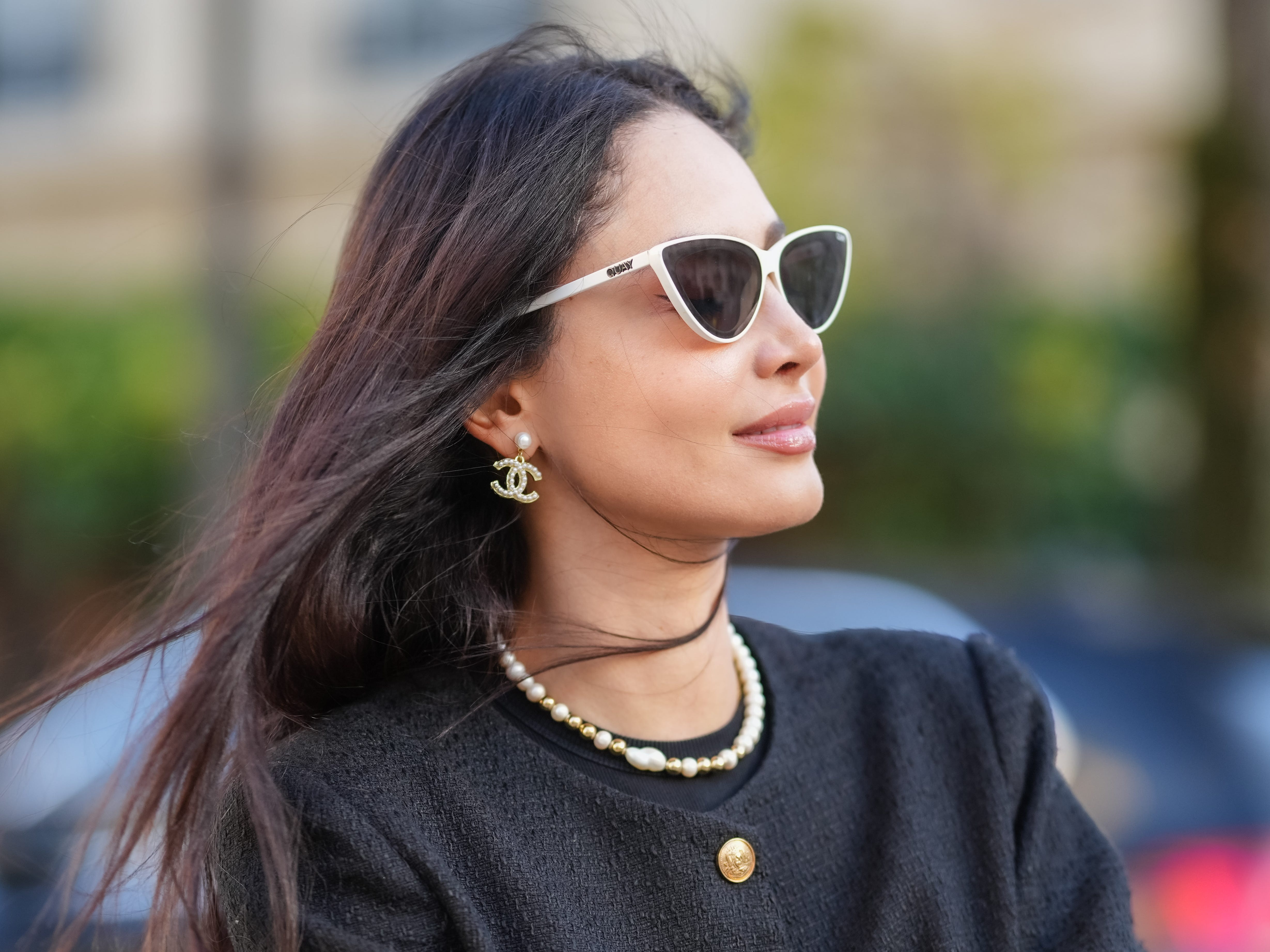 woman on the street wearing a chic black outfit with channel earrings and white sunglasses