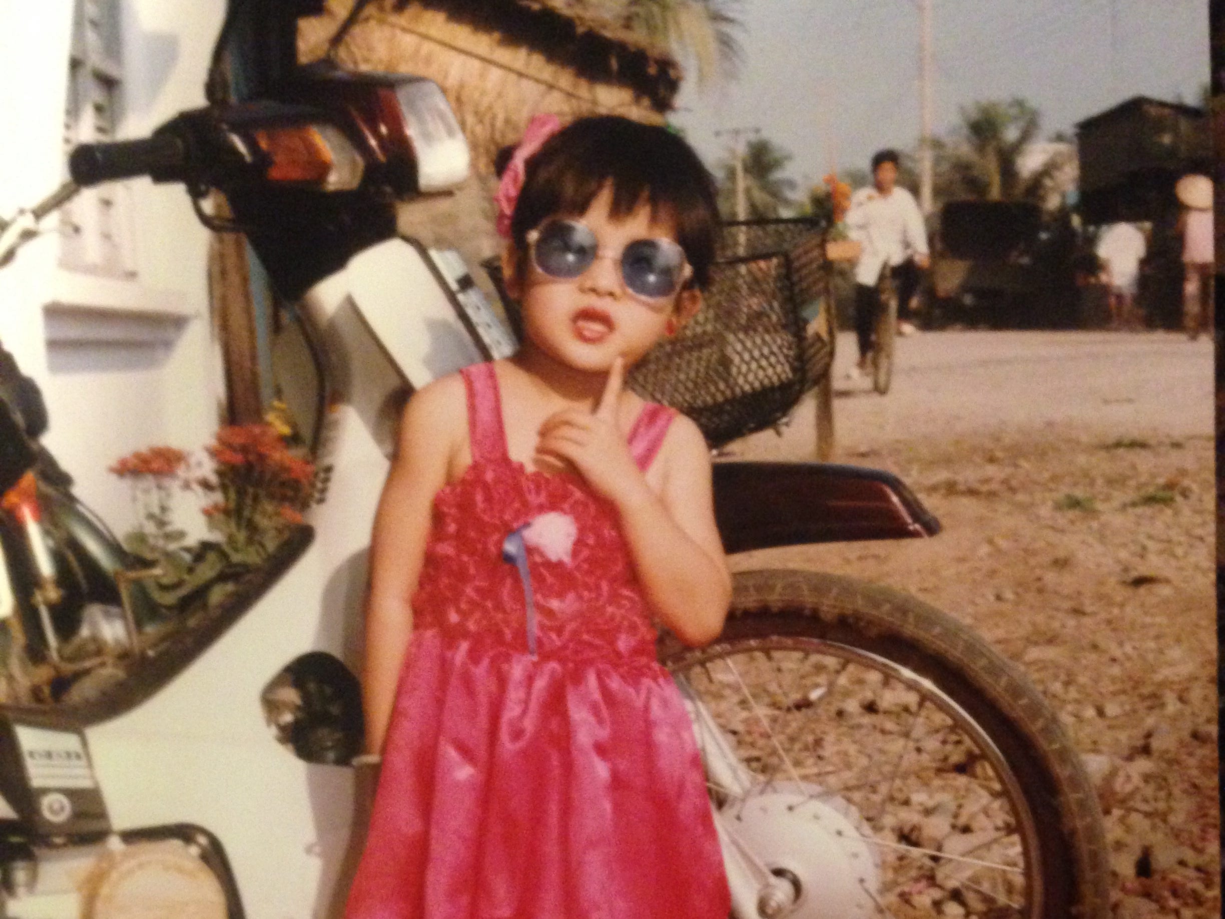 A little girl in a red dress standing by a motorbike in Vietnam in the 1980s.