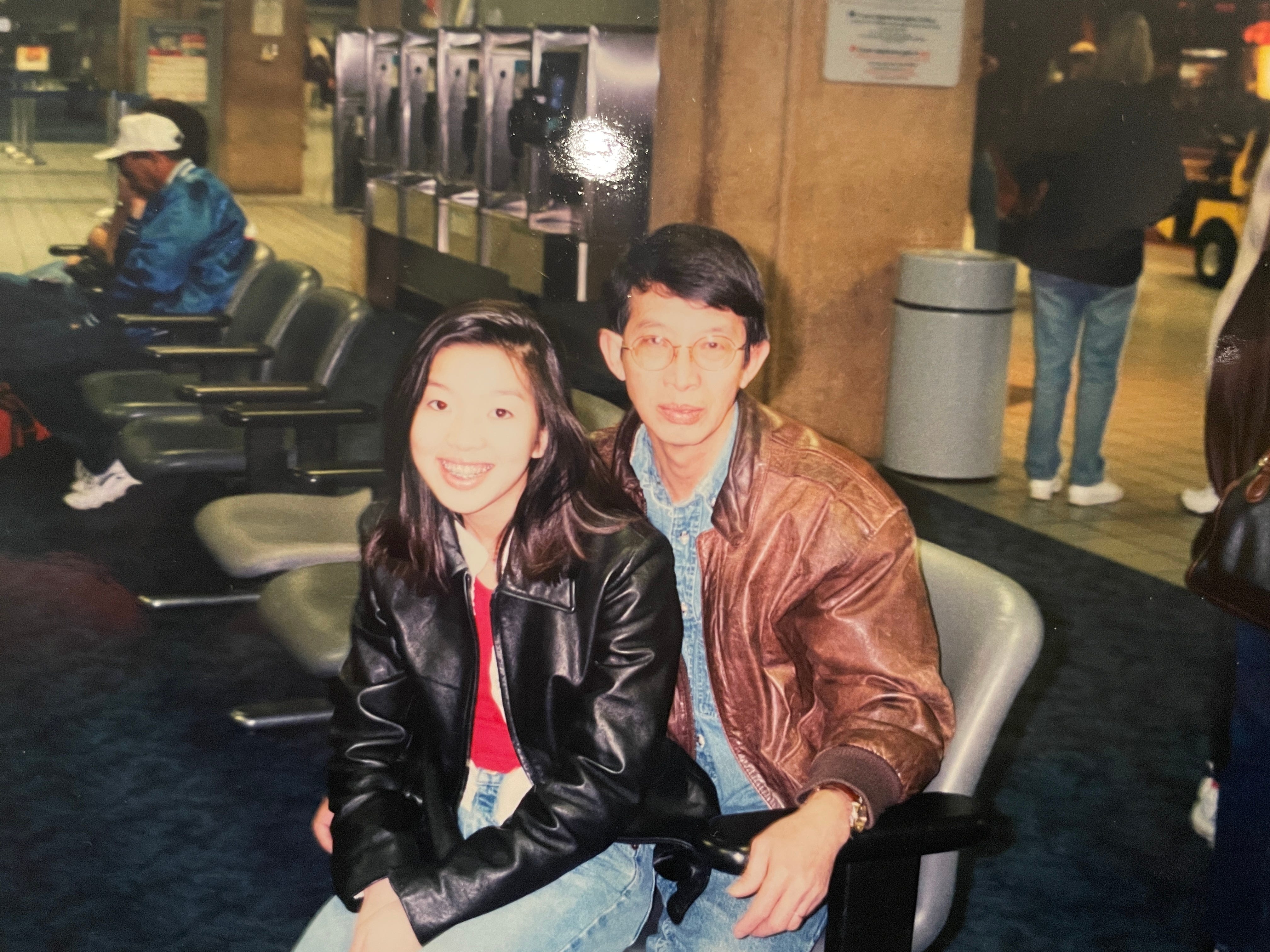 Young girl with red shirt and black leather jacket sitting on a man's lap.