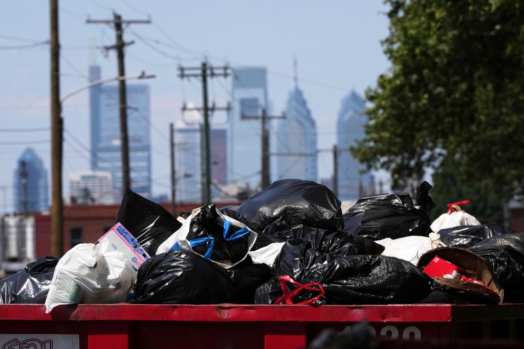 Garbage fills up a container as the Philadelphia skyline is seen in the background.