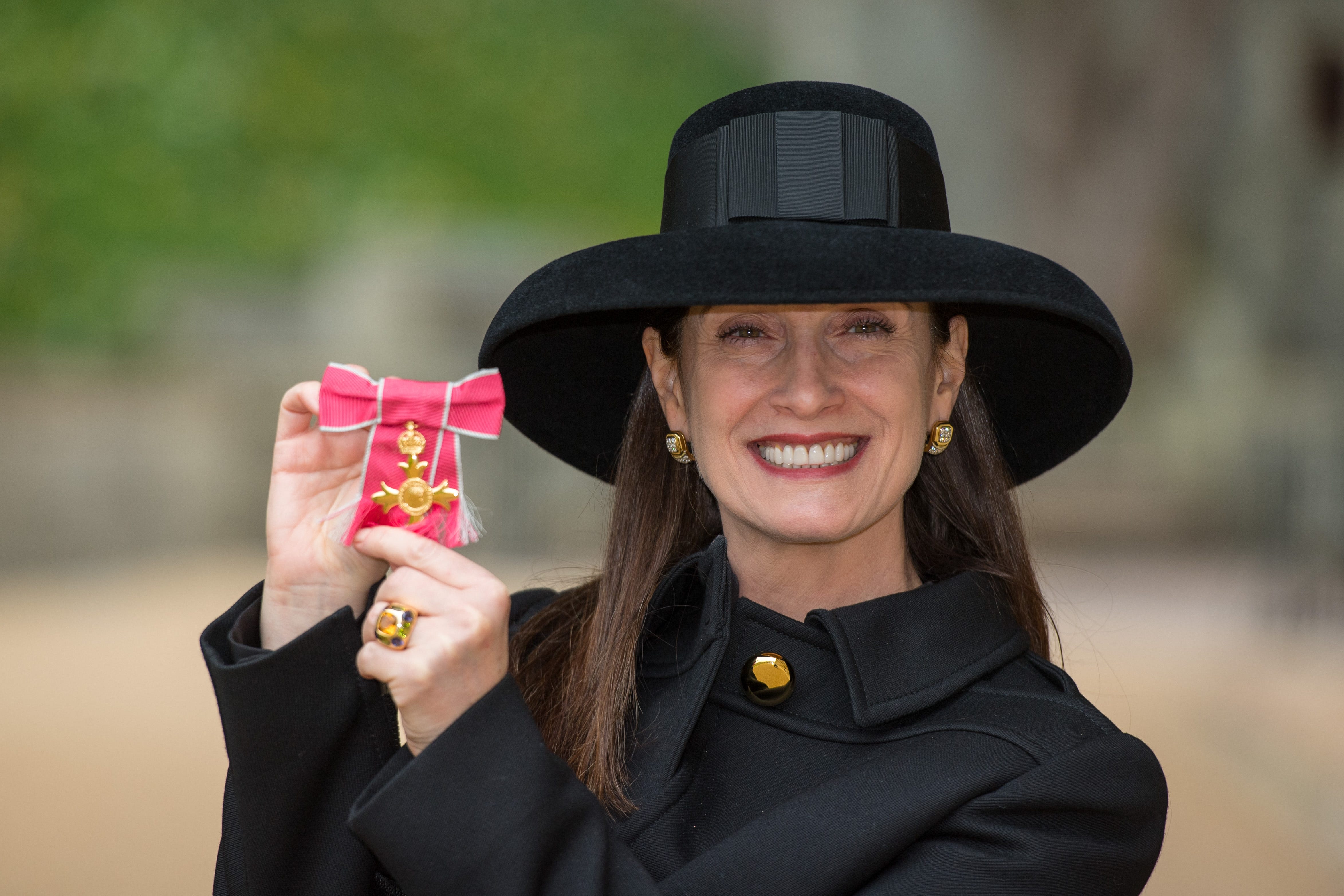 A woman holds a red ribbon and gold cross wearing black