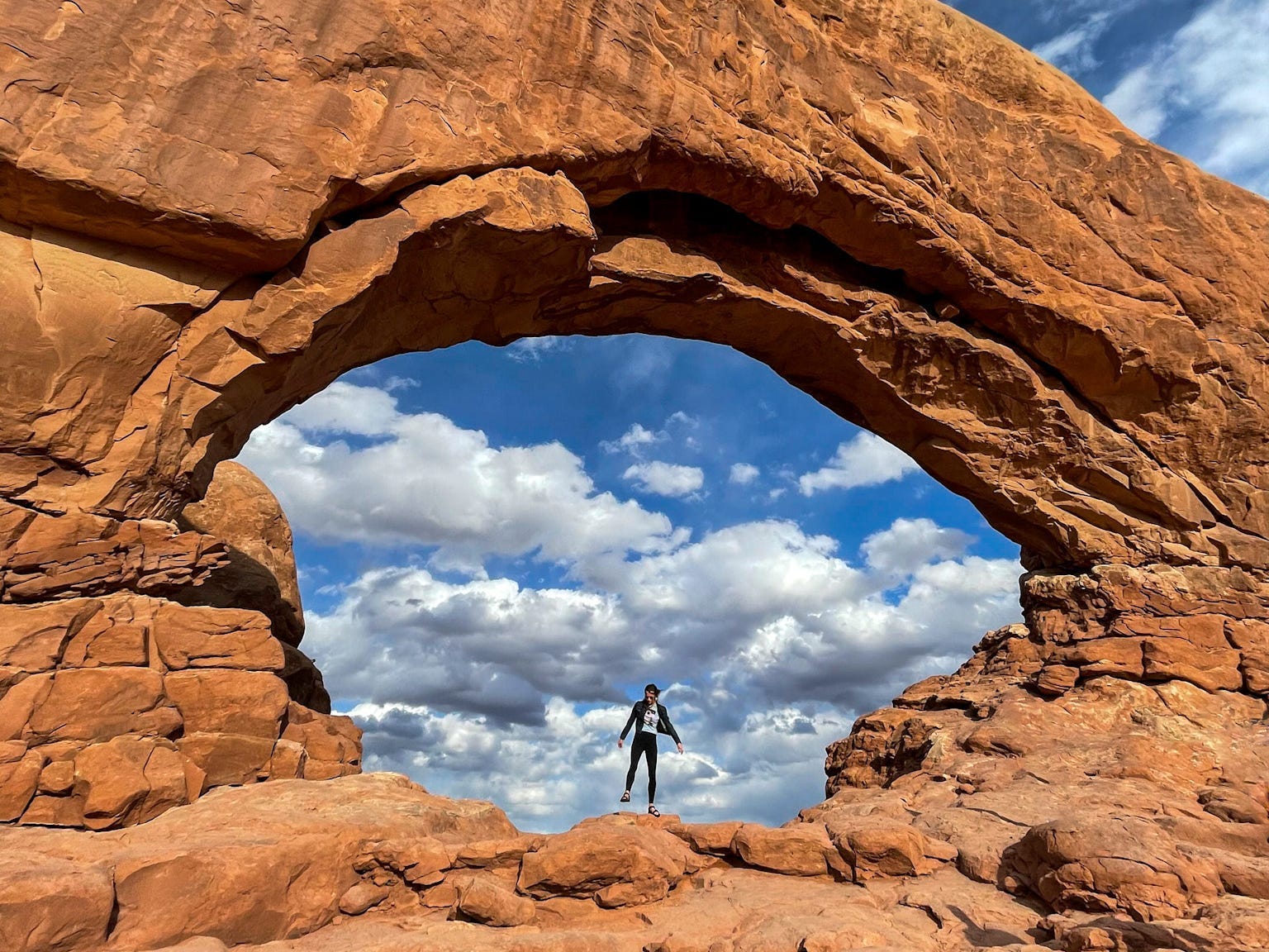 Emily stands under a sandstone arch at Arches National Park.