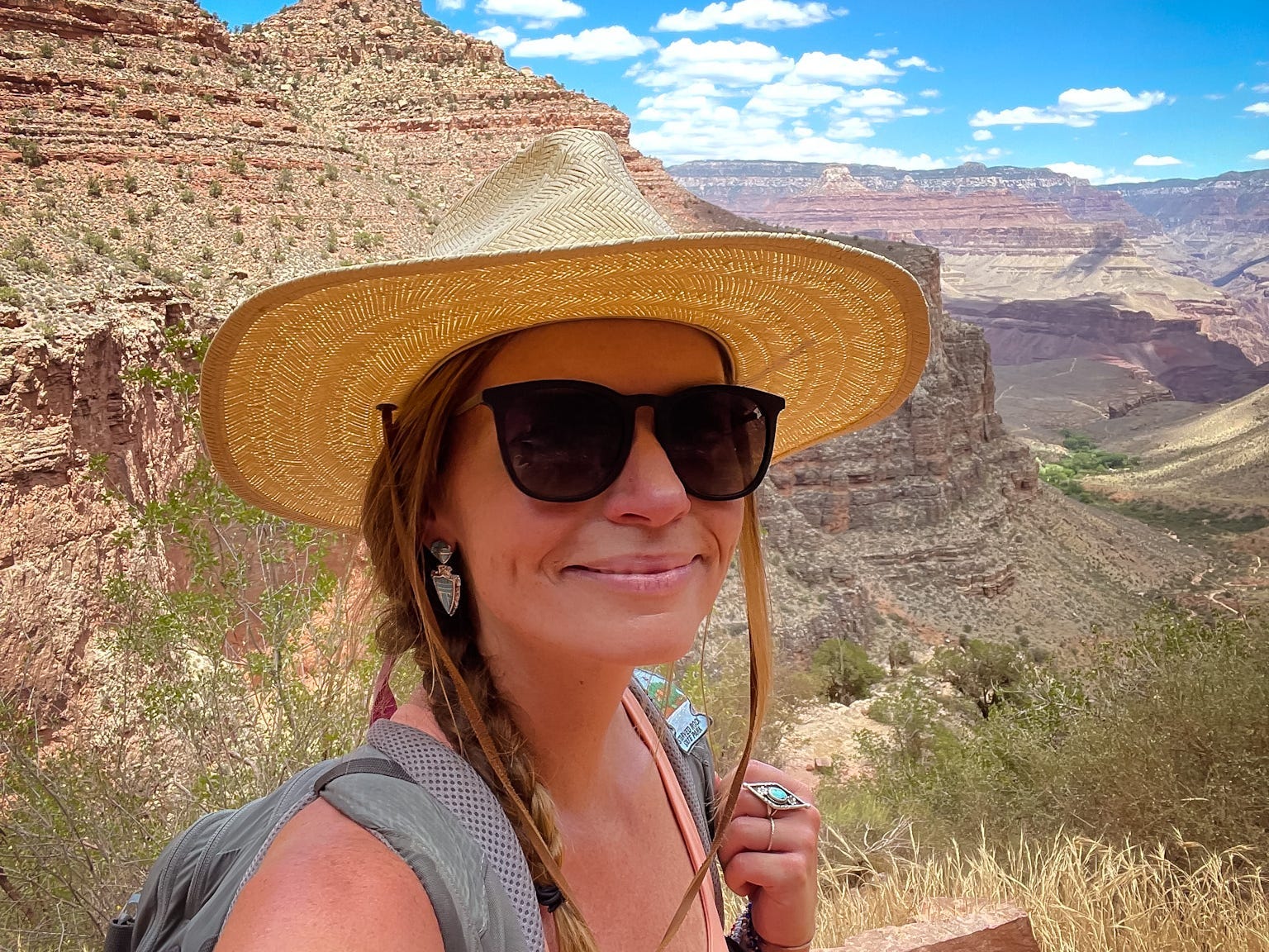 Emily takes a selfie with the Grand Canyon behind her, wearing sunglasses and a straw hat.