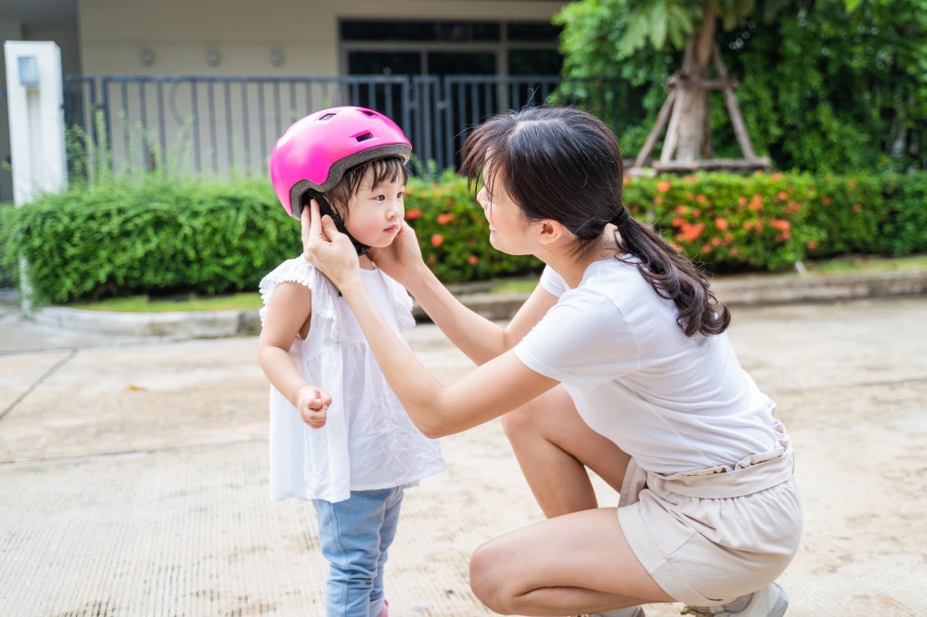 A mother putting a pink helmet on her young daughter.