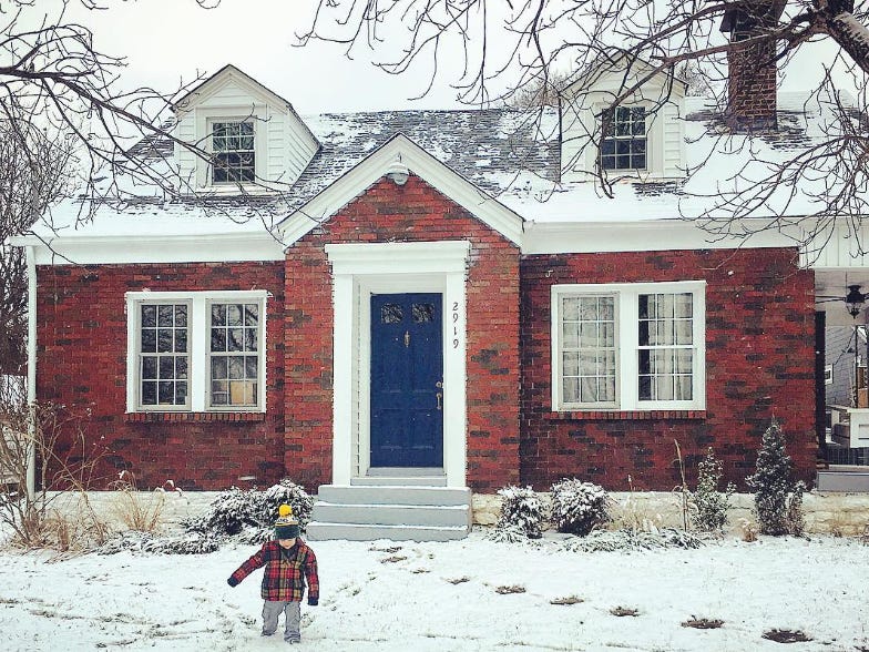 House with snow on its roof, lawn, and a kid out front