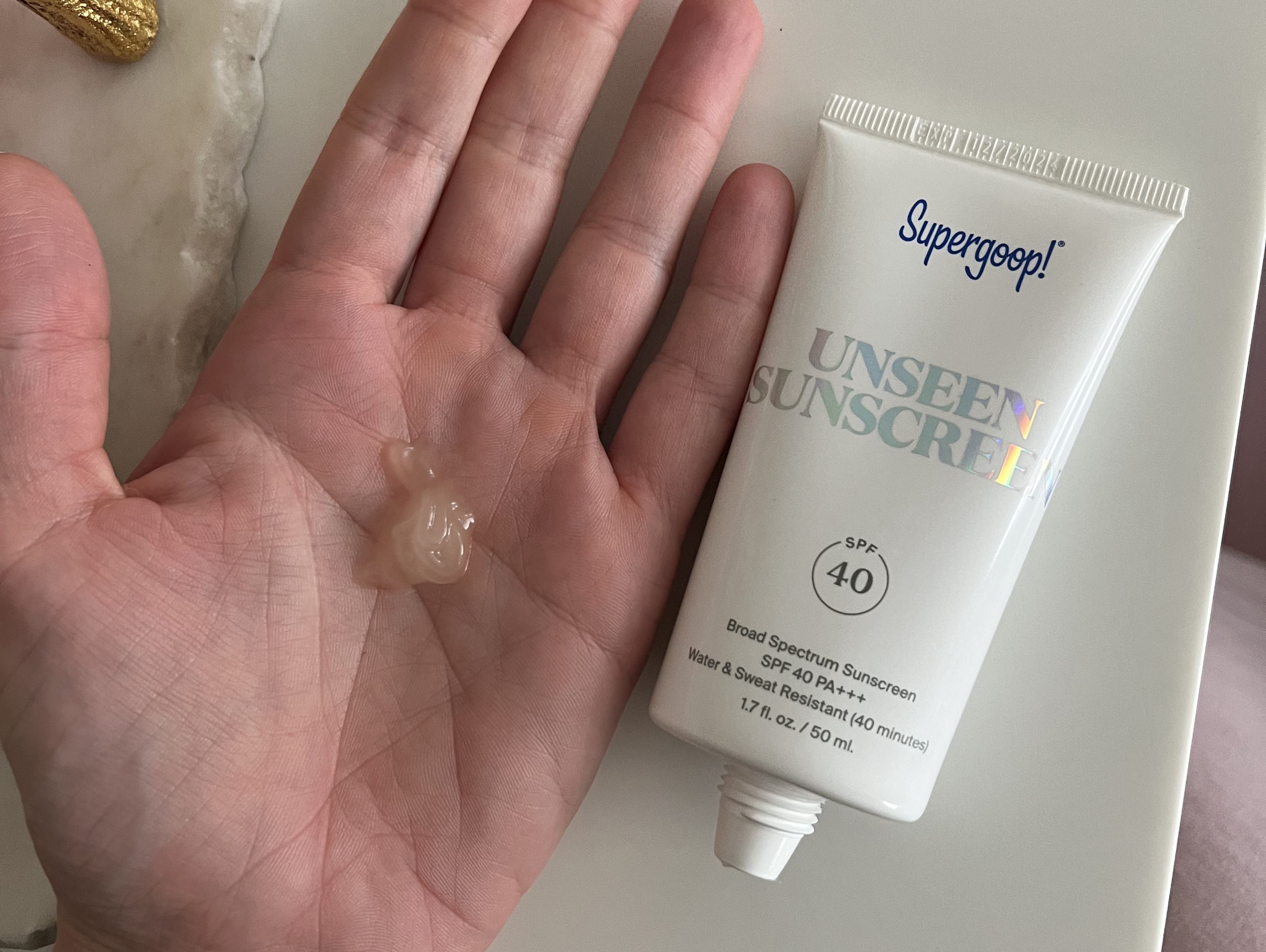 Dollop of sunscreen on author's palm with Supergoop bottle next to it.