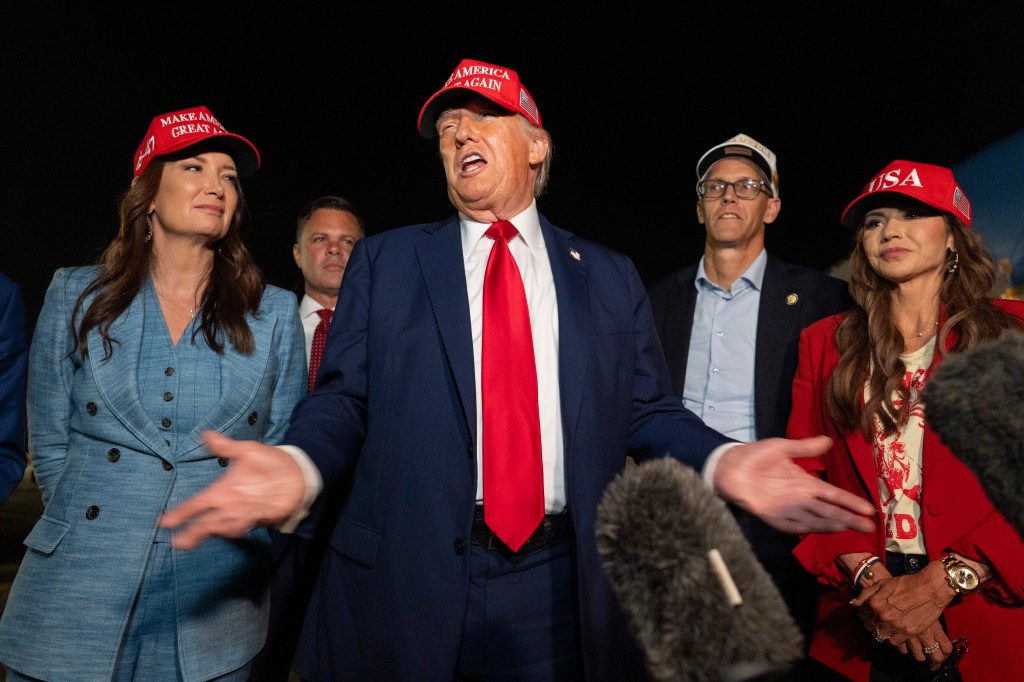 Donald Trump speaking to reporters, flanked by several other individuals.