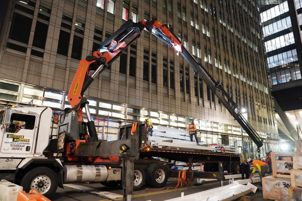 Workers unloading steel beams at a construction site at night.