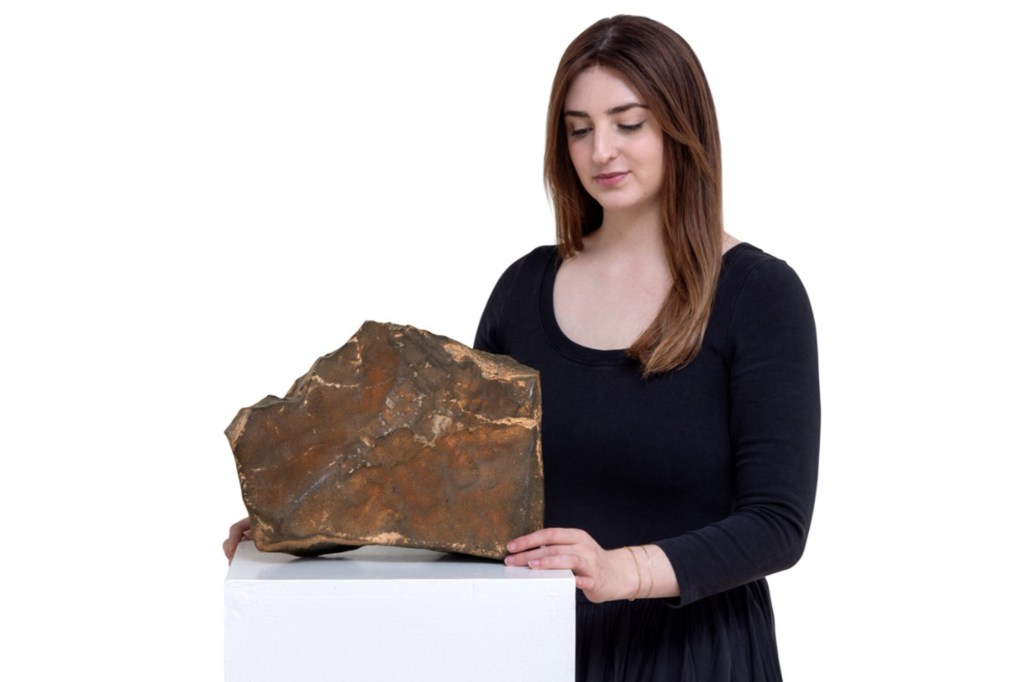 Woman presenting a large, irregularly shaped brown rock.