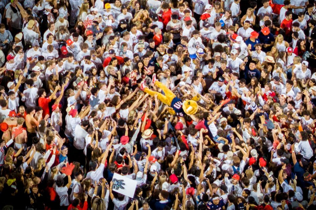 A large crowd of people lifting a mascot into the air.