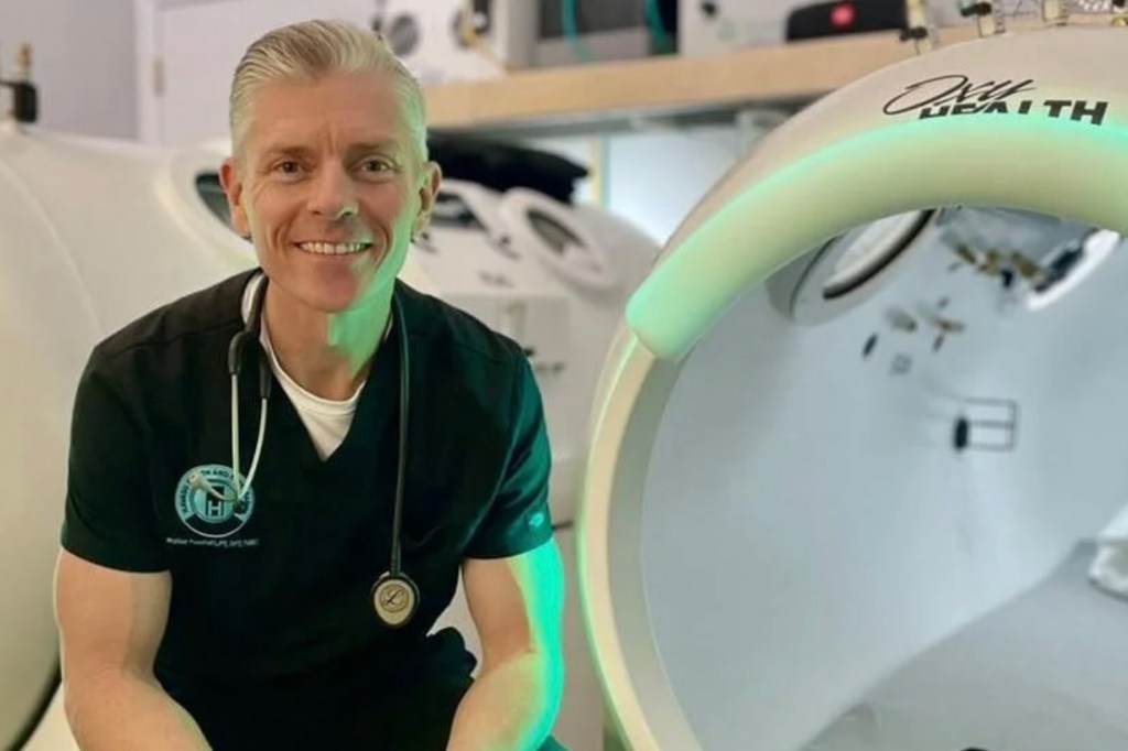 A doctor sits in front of a hyperbaric chamber.