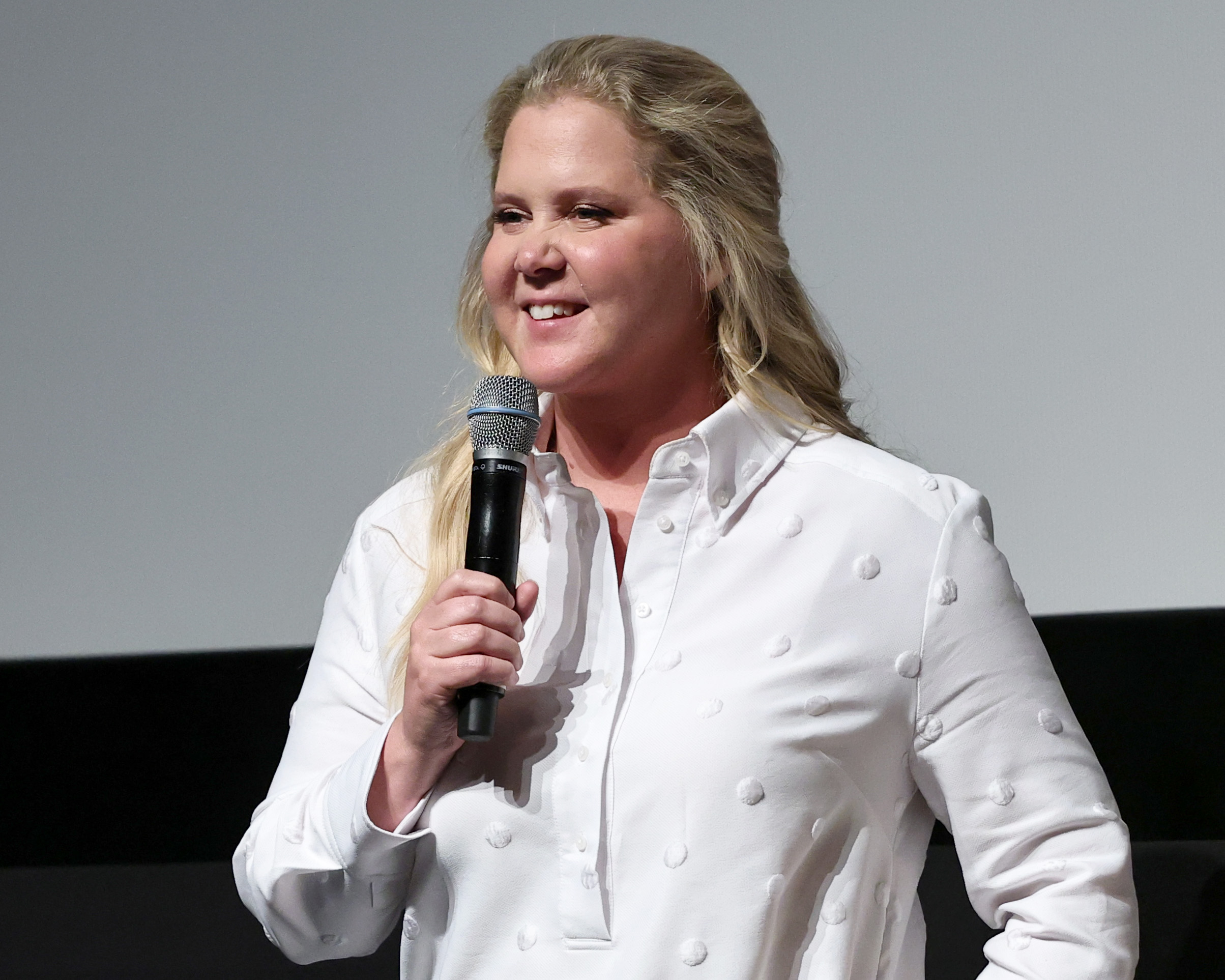 Amy Schumer with a mic in a white shirt. 
