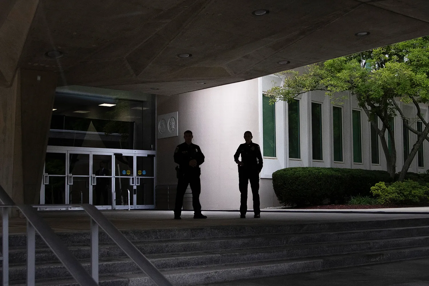 Two officers are seen silhouetted as they stand on the top of stairs under an overhang outside an office building.