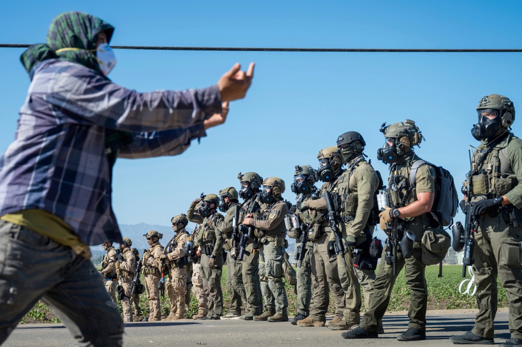 Protester facing a line of armed officers in gas masks during an immigration raid.