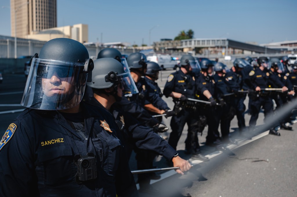 Police officers in riot gear stand in a line during a protest.