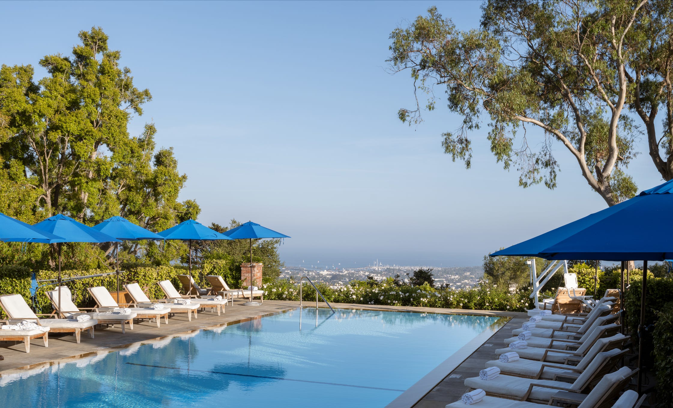 Hotel pool lined with chairs overlooking the city in the distance.