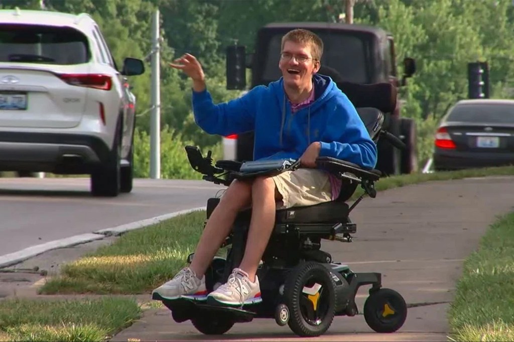 Man in wheelchair waving to cars.
