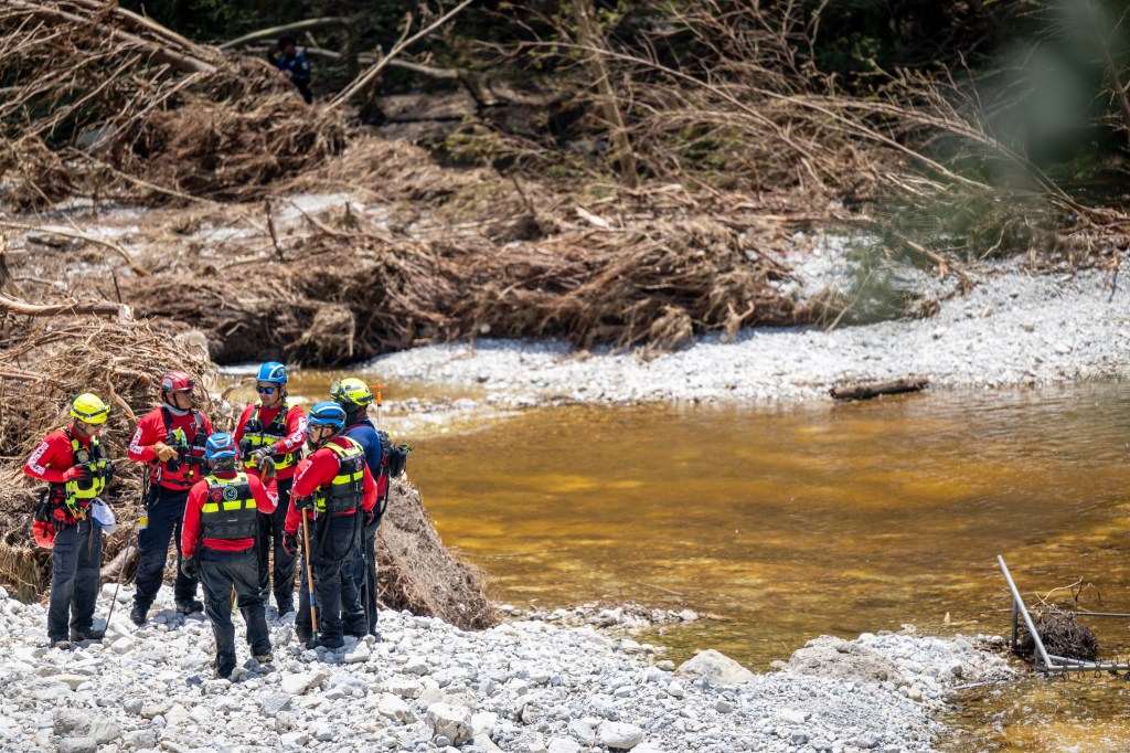 Rescue workers assessing flood damage by a river.