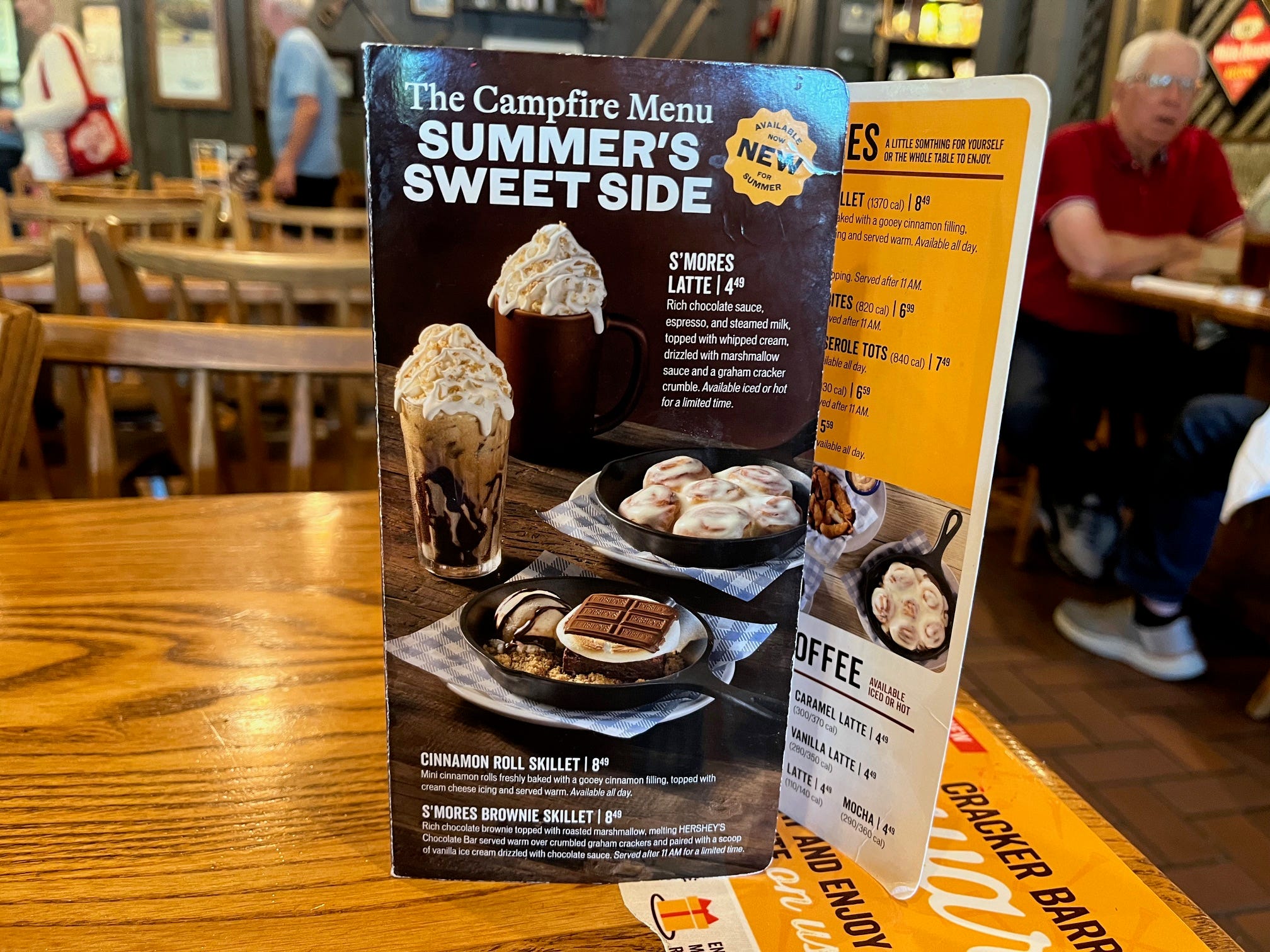 A menu on the table at a Cracker Barrel restaurant highlights new menu items including the S'mores Latte and the Cinnamon Roll Skillet.
