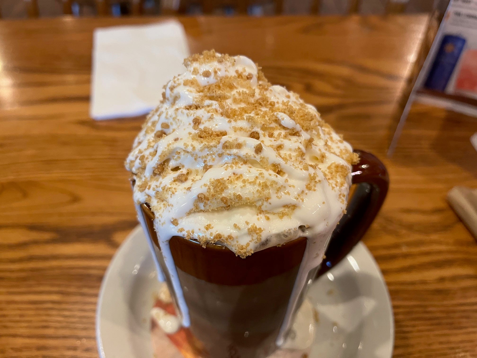 A smores latte with whipped cream and graham-cracker crumbs sits in a brown ceramic mug at a Cracker Barrel