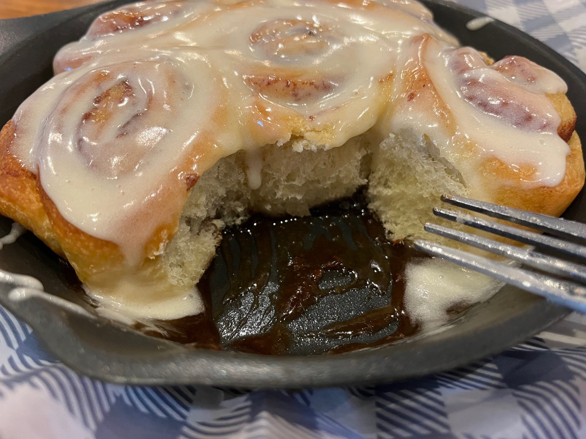 Sauce from the cinnamon rolls sits in the bottom of a cast-iron skillet at Cracker Barrel as the author's fork rests on the side of the skillet.
