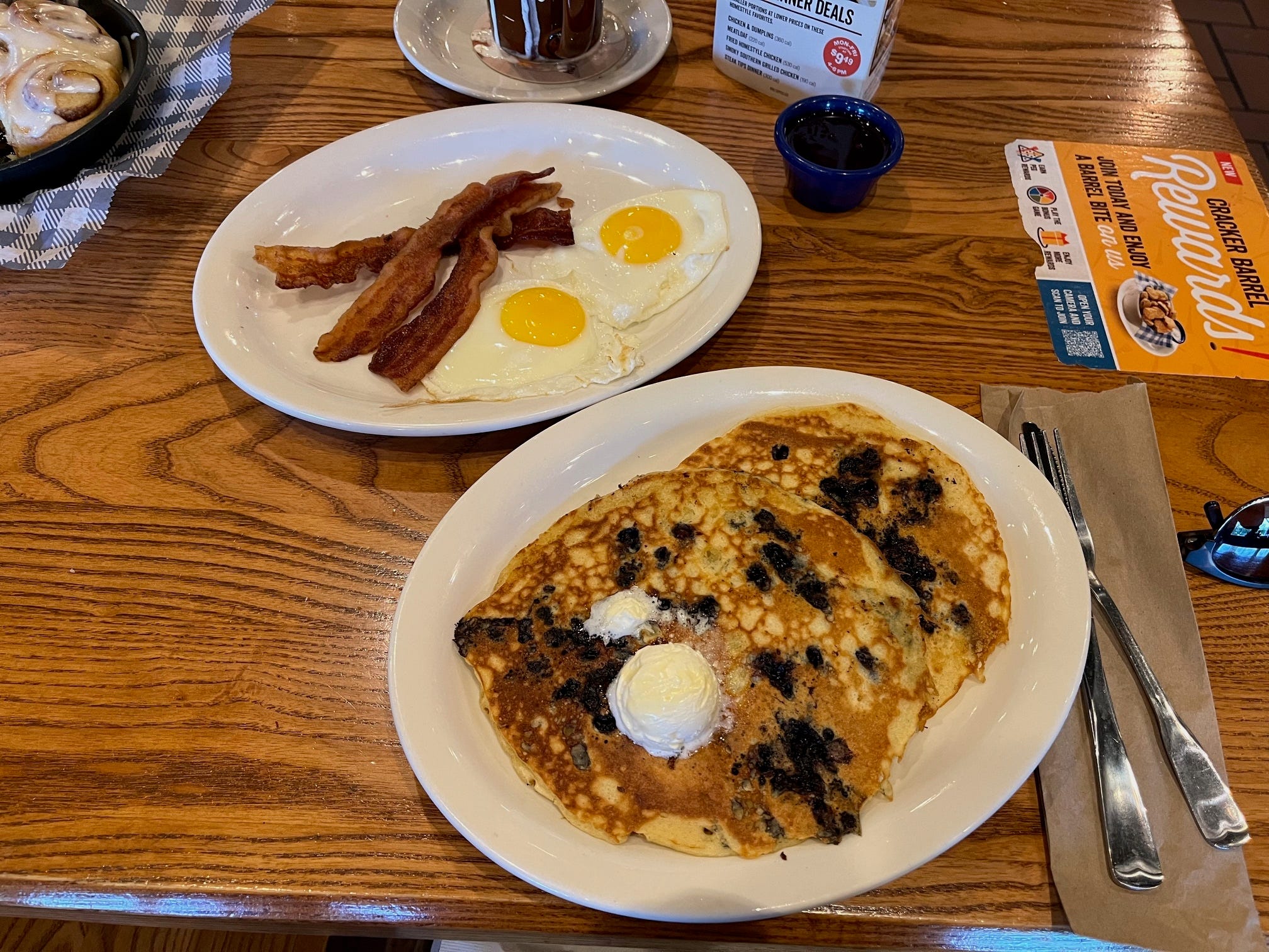Blueberry pancakes, sunny-side up eggs, and three strips of bacon sit on a table at Cracker Barrel