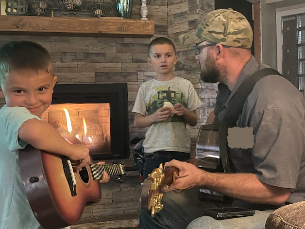 The author's husband sitting at home playing guitar with their kids.