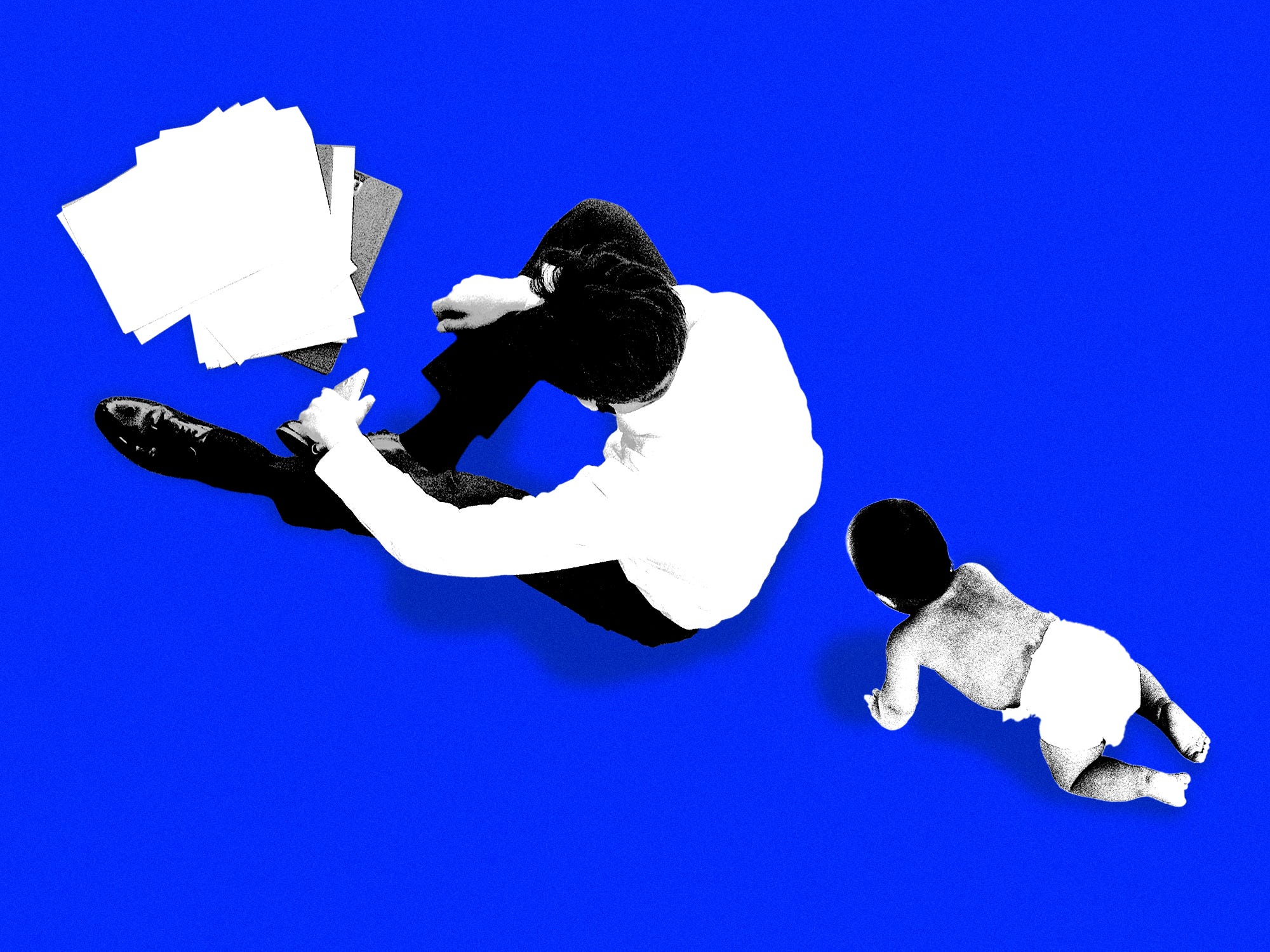 A father sitting in front of paper work while his child crawls towards him from behind