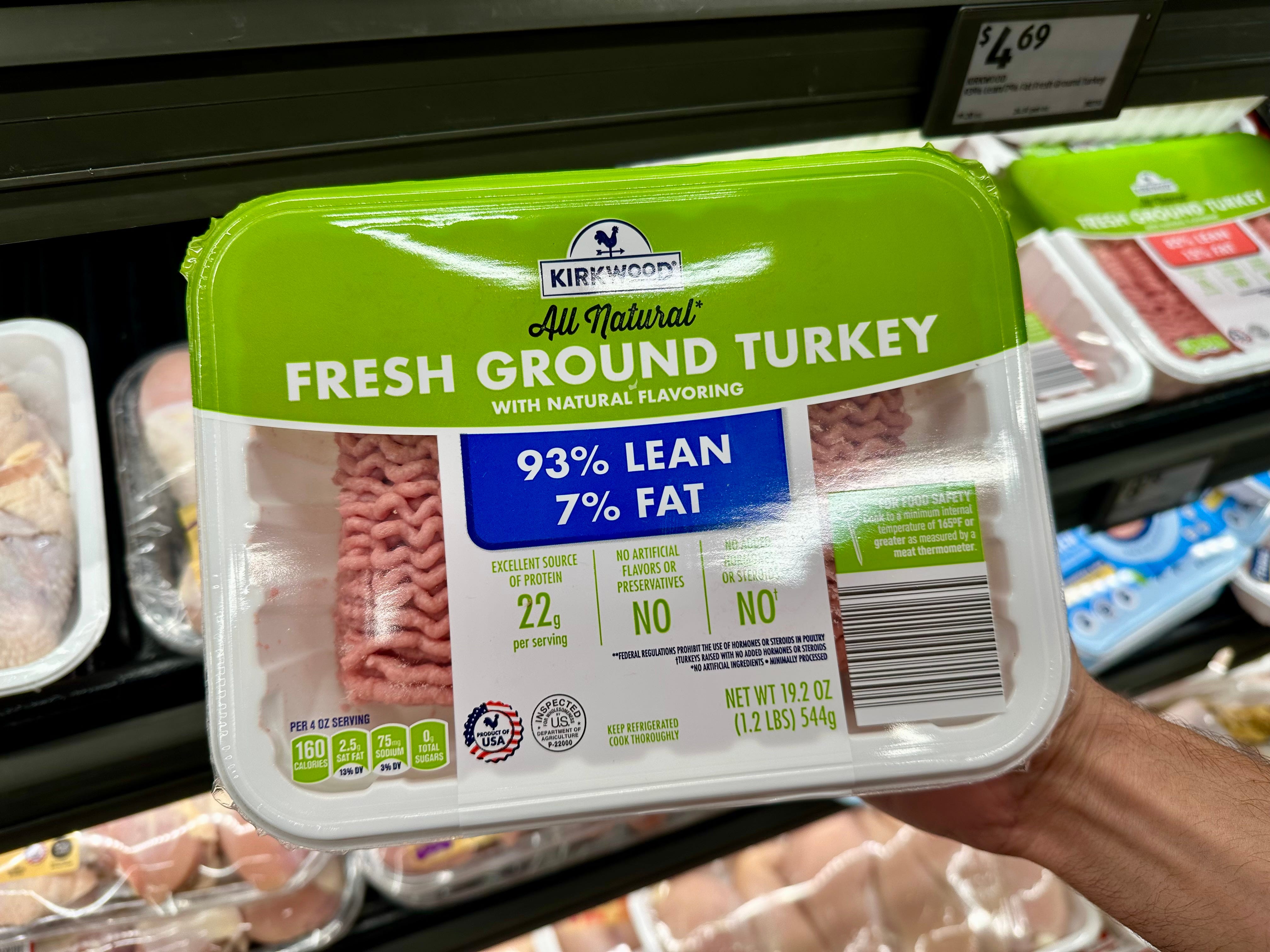 A hand holding a package of Kirkwood all-natural fresh ground turkey.