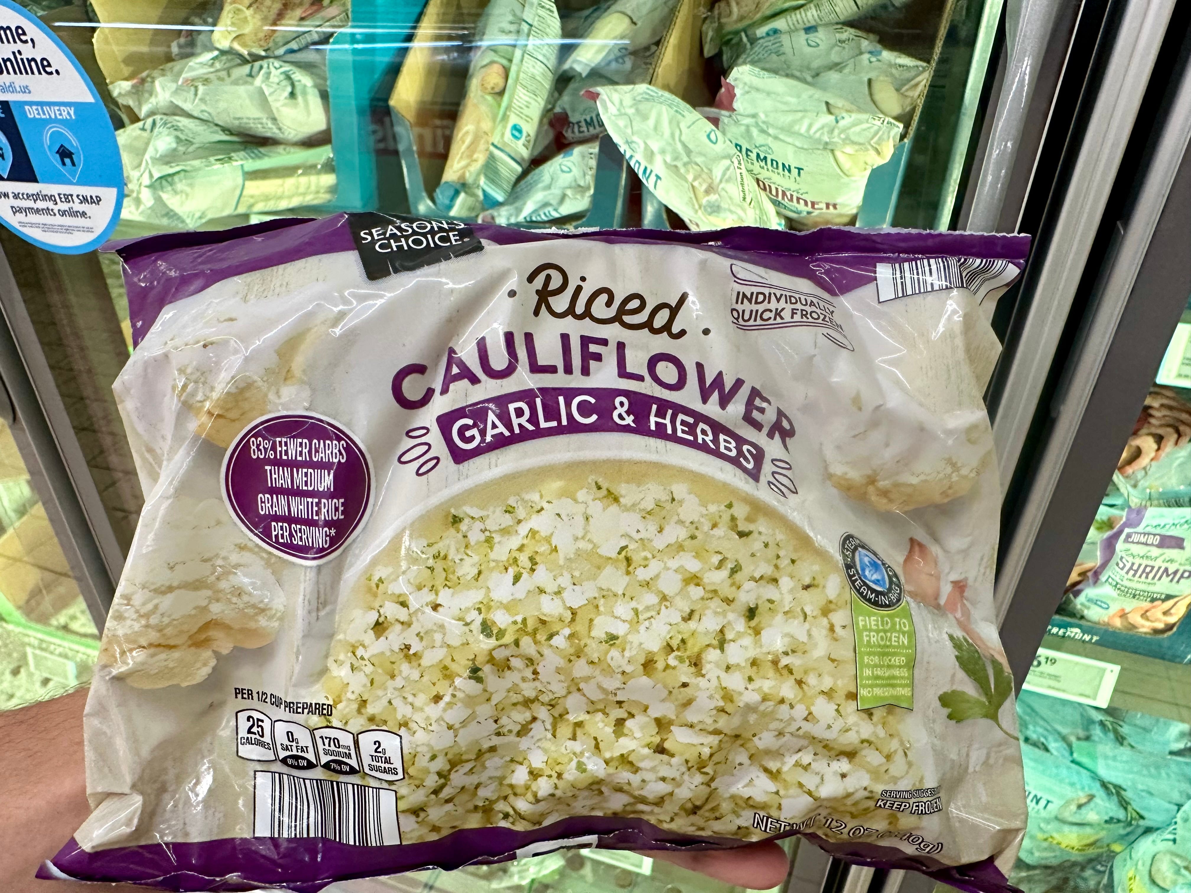 A hand holding a bag of riced cauliflower with garlic and herbs.