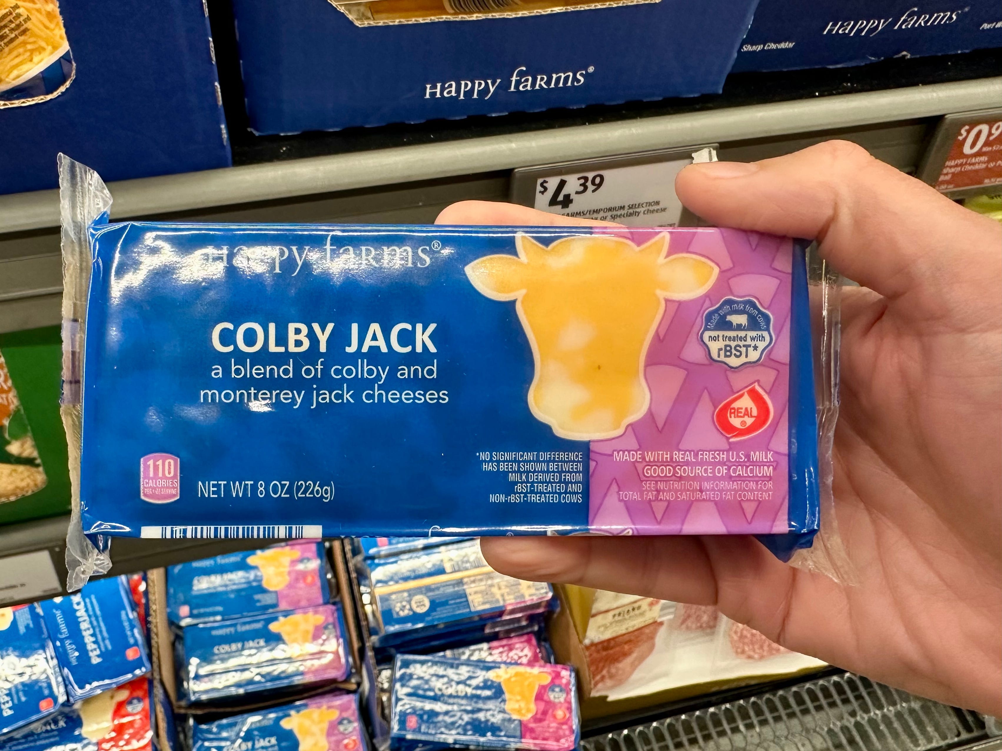 A hand holding a package of Happy Farms colby jack.