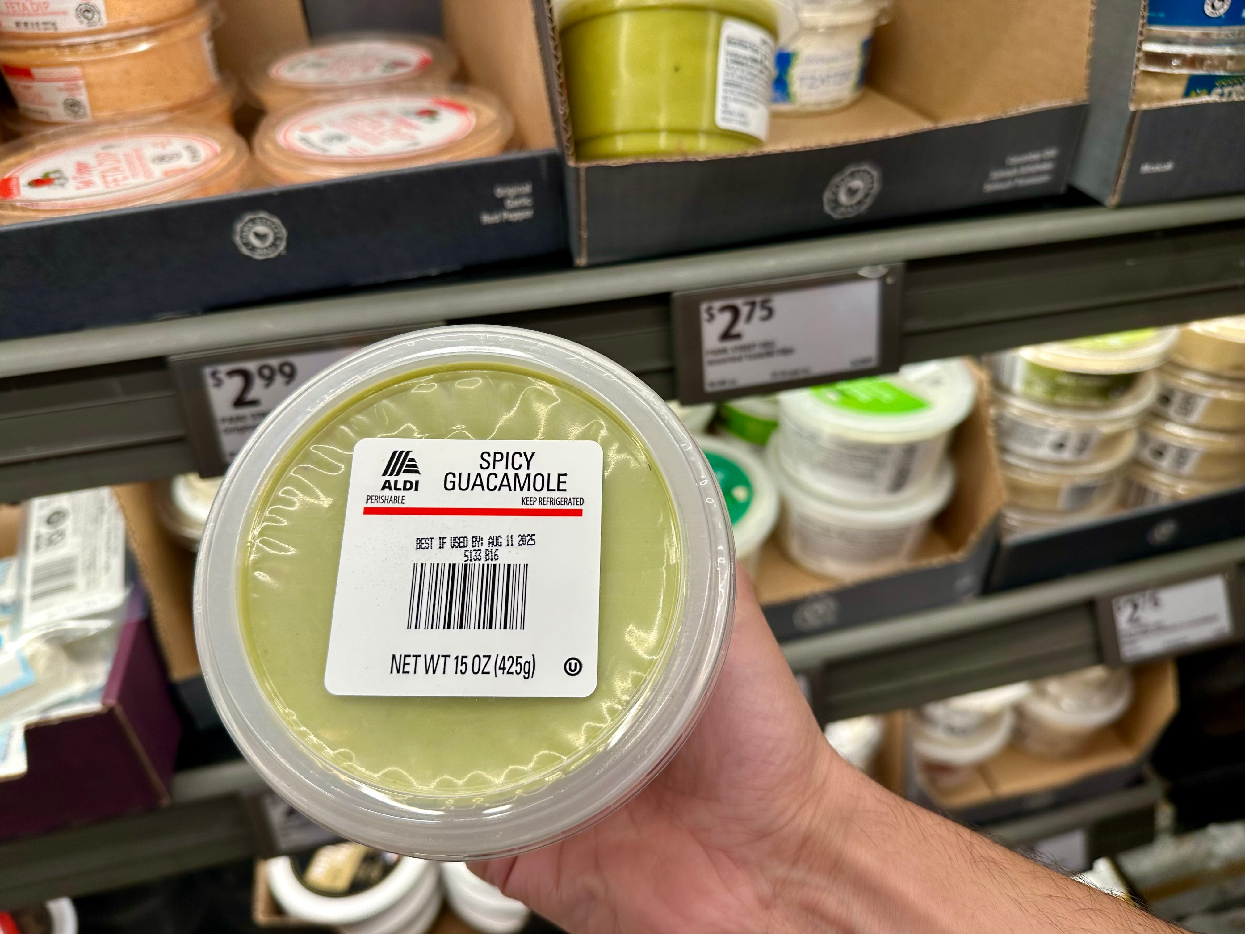 A hand holding a container of Aldi spicy guacamole.