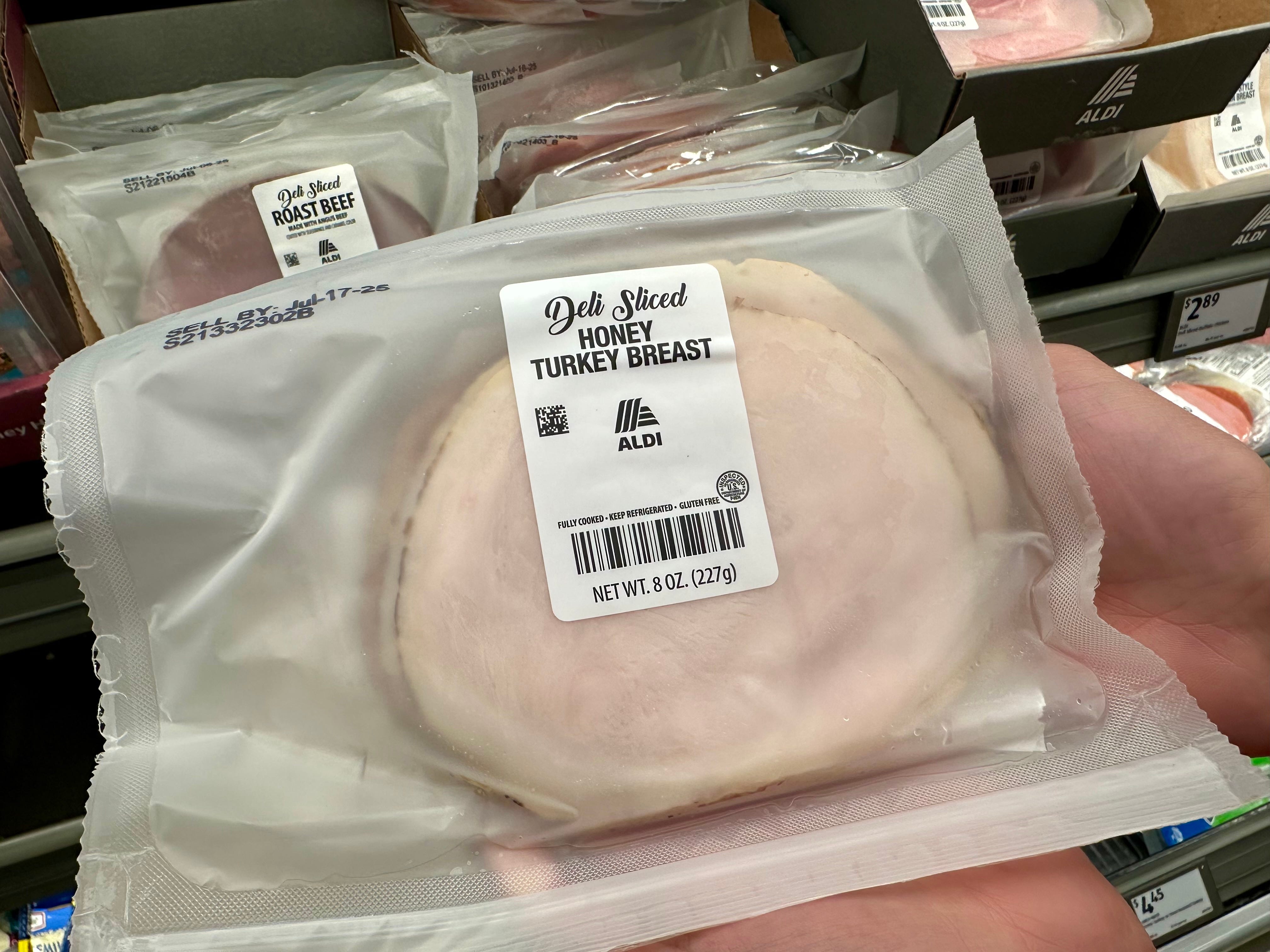 A hand holding a package of Aldi deli-sliced honey turkey breast.