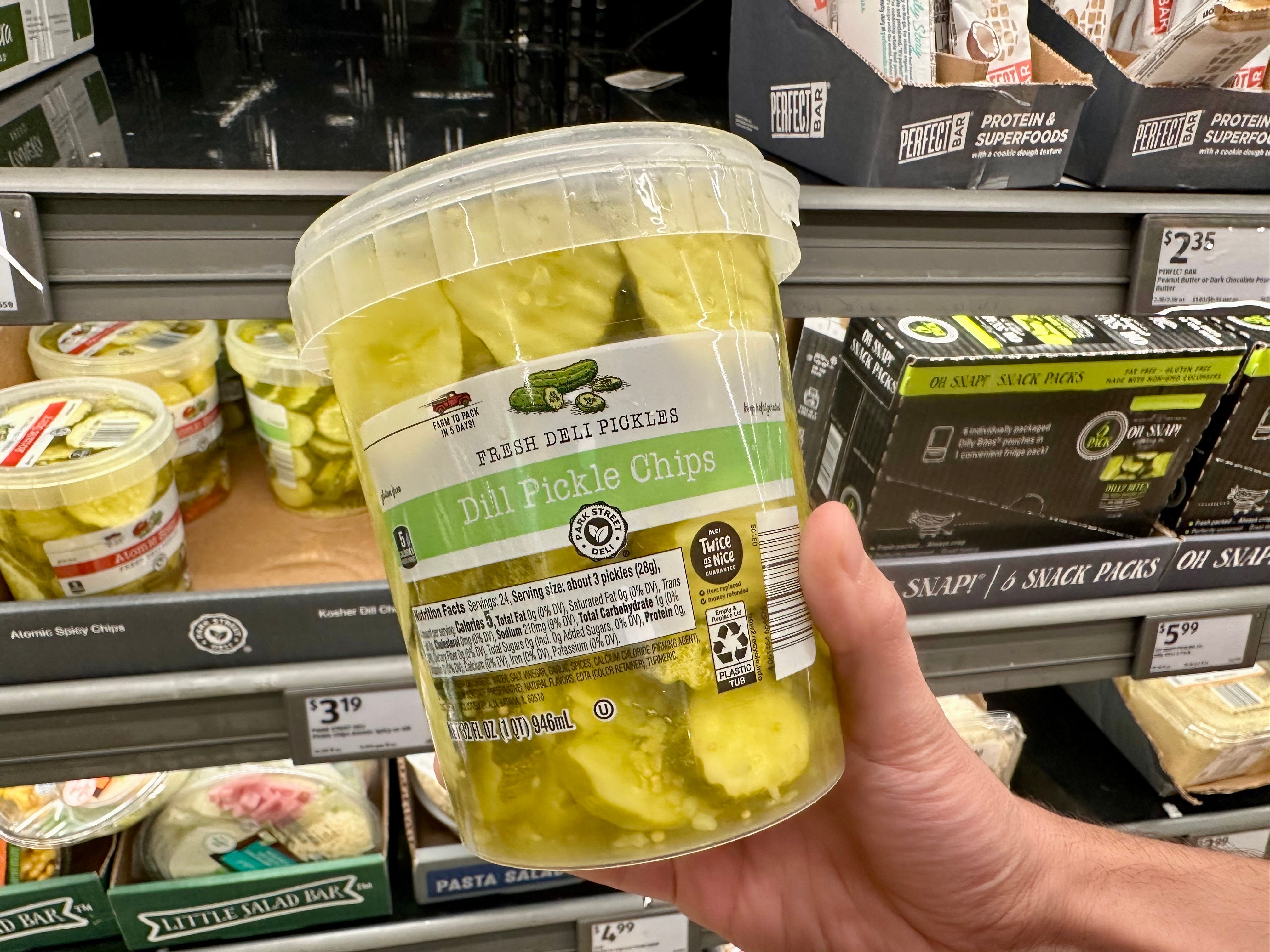 A hand holding a container of dill pickle chips.