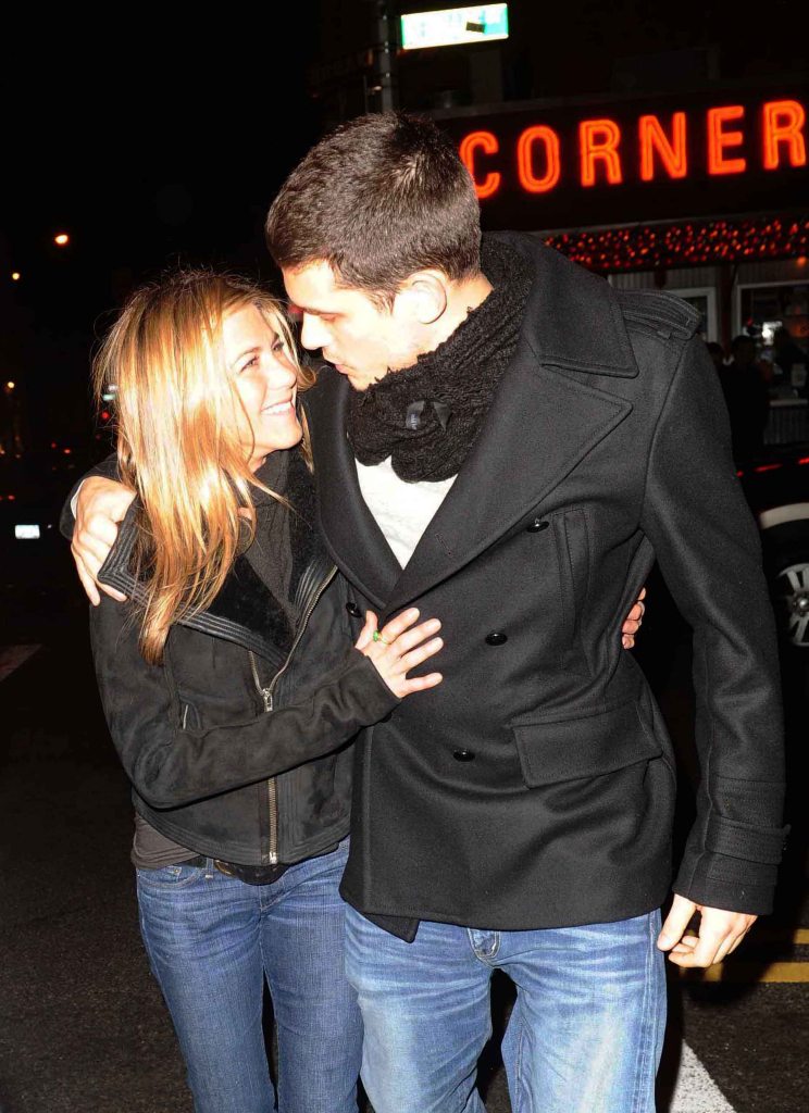 Jennifer Aniston, in a black jacket and jeans, cuddles up to John Mayer, in a black jacket and jeans and white t-shirt.